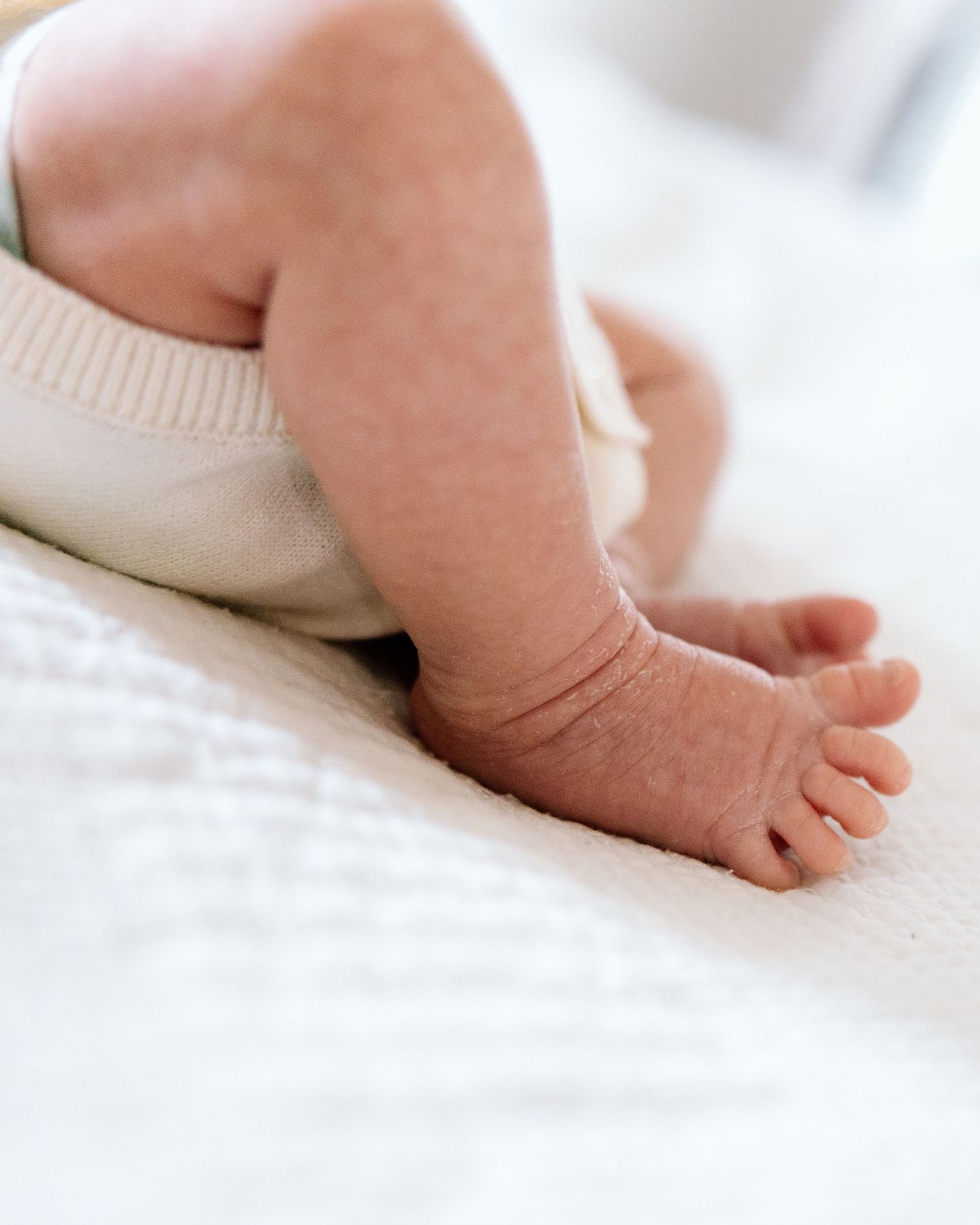 Close-up of a newborn baby's tiny feet and legs resting on a soft white textured blanket.