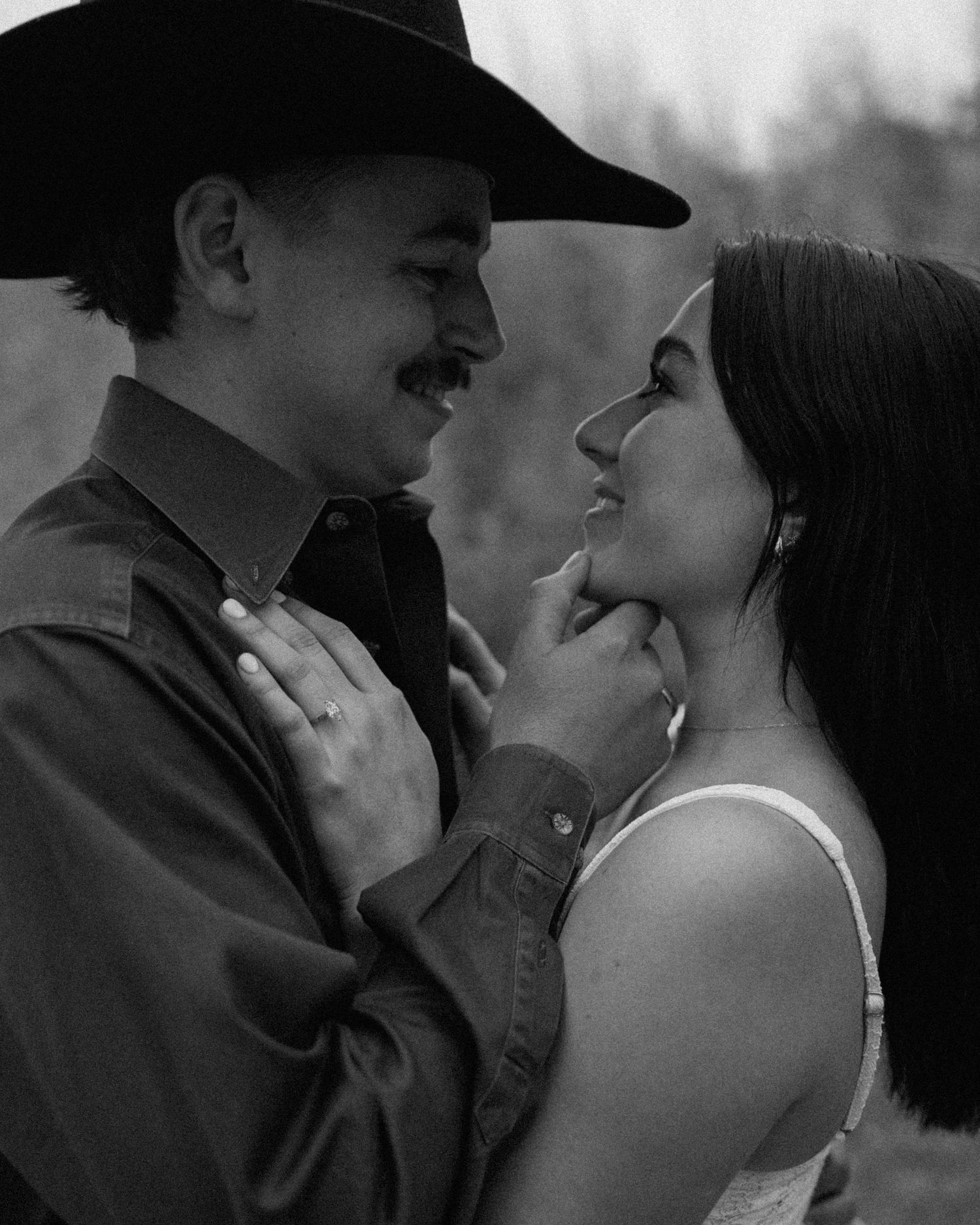 Black and white photo of a couple in an intimate moment, man in cowboy hat gently holding womans chin.
