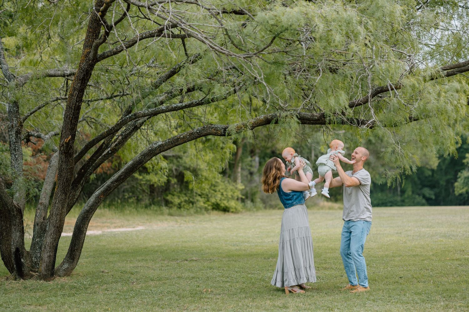 Two people stand beneath a willow tree in a grassy meadow on a sunny day holding something carefully.