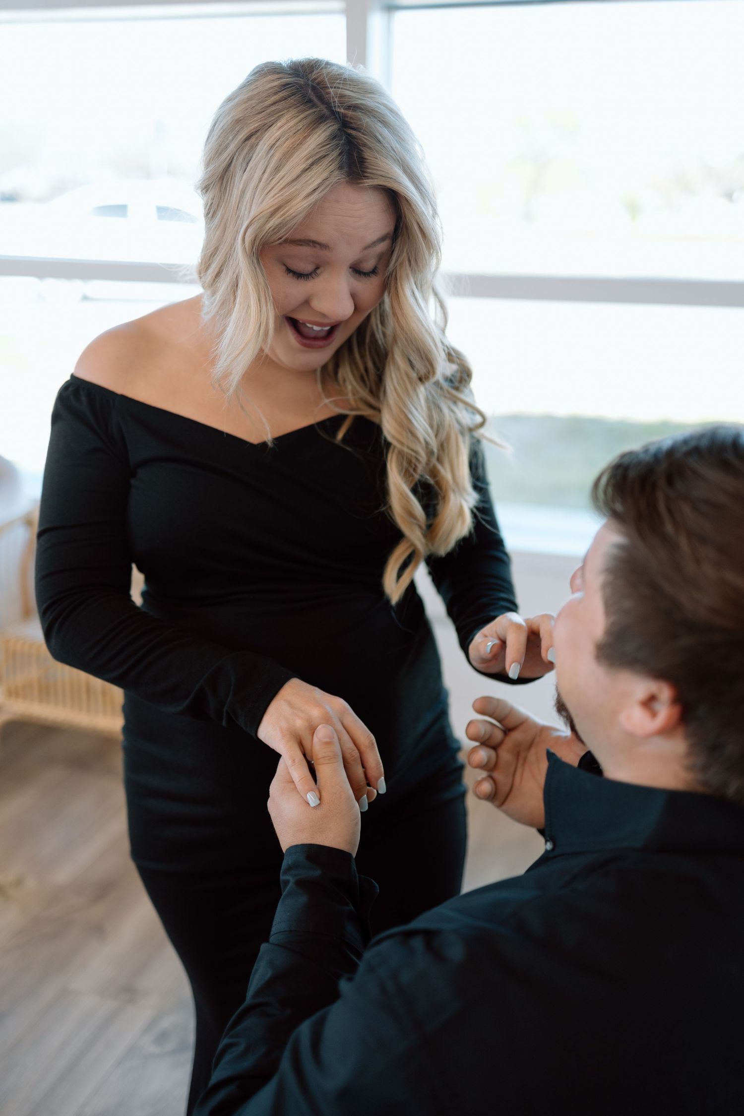 A romantic proposal scene shows someone in a black sweater kneeling while holding up a ring to a person in a black dress.