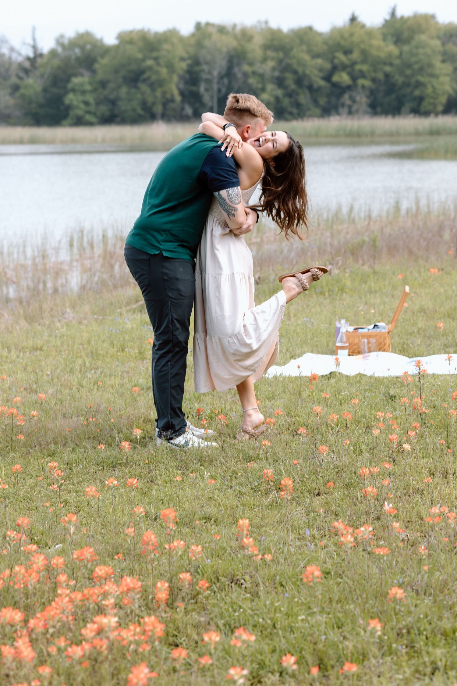 A couple shares a romantic dip pose in a field of orange wildflowers by a lake.