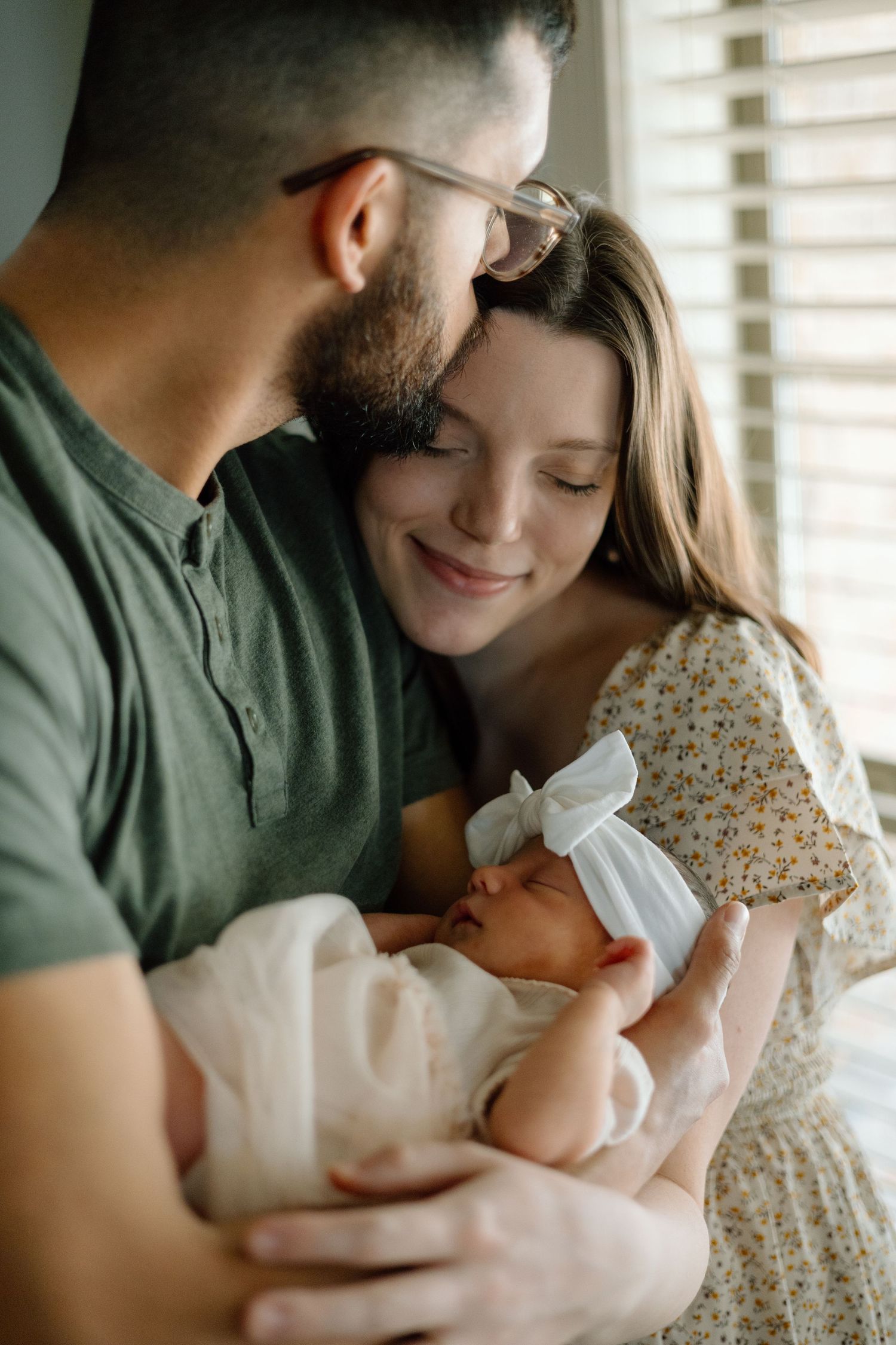 Tender moment between parents looking at their newborn baby near a window.