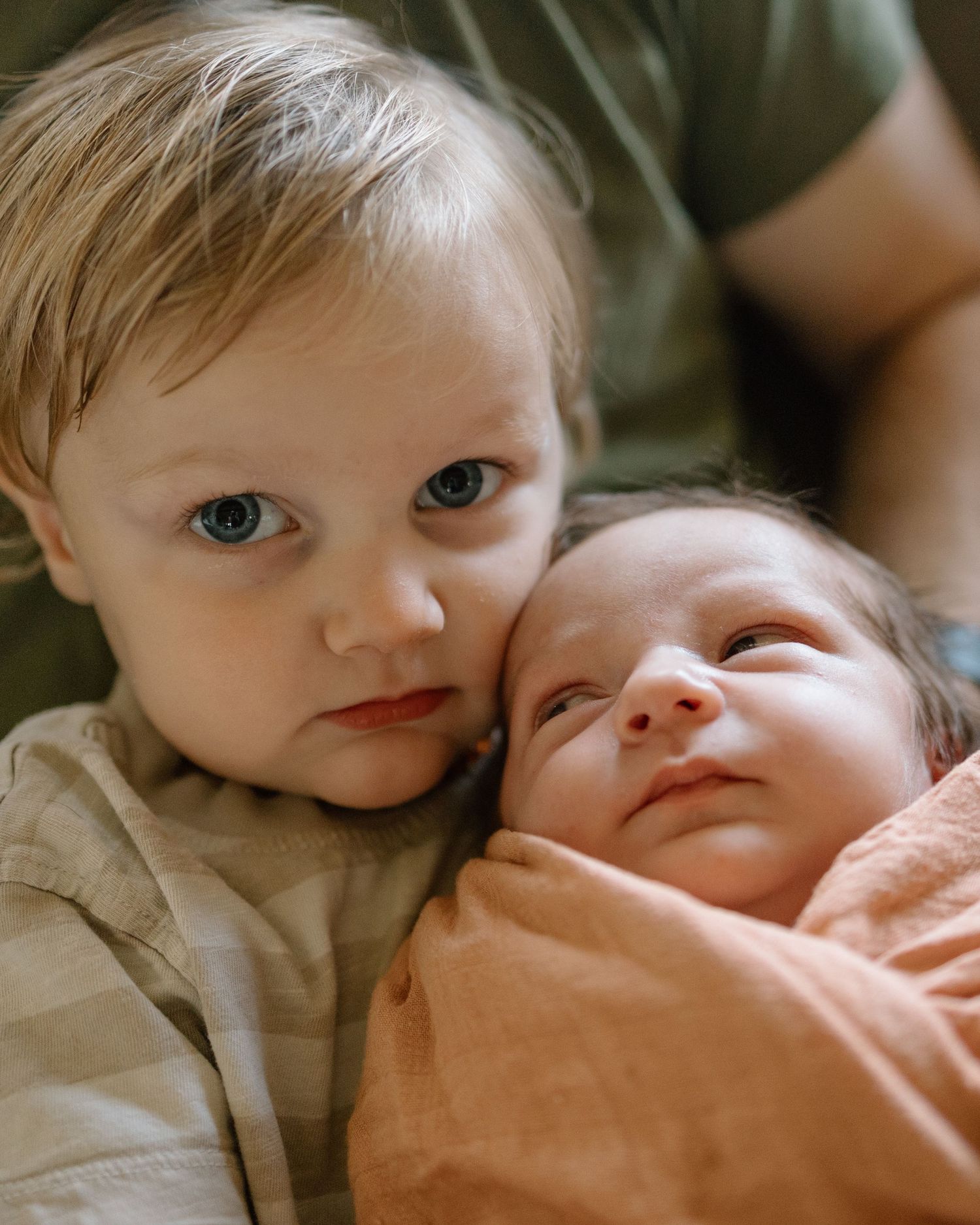 Two young children in a close-up photograph, one wearing light colored clothing and one wrapped in a peach blanket.