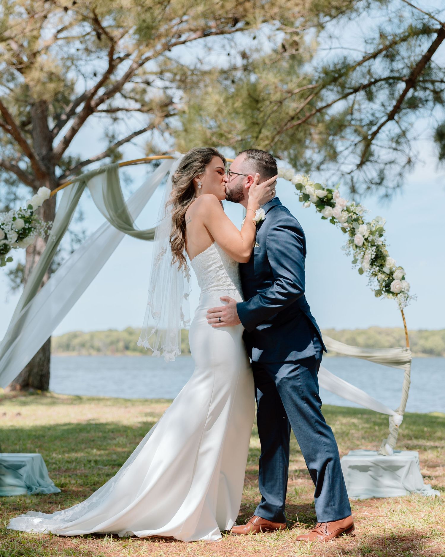 A romantic kiss during an outdoor waterfront wedding ceremony.