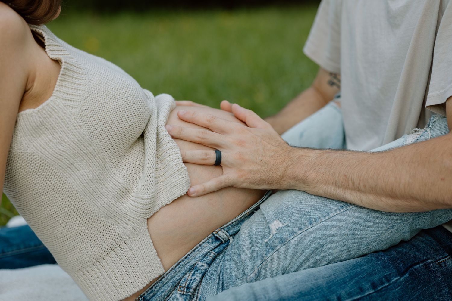 Tender maternity moment with hands cradling baby bump in white knit sweater and jeans.