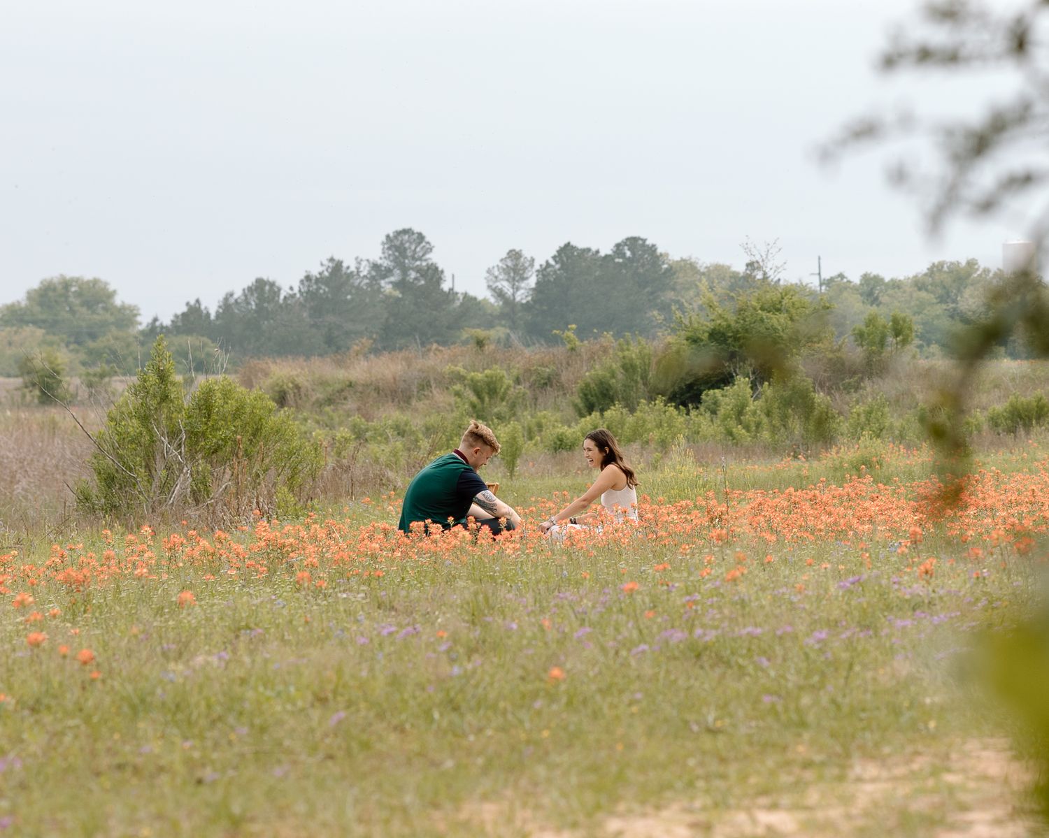 Two figures sitting in a field of orange wildflowers surrounded by trees and grass documentary photography college station Texas.