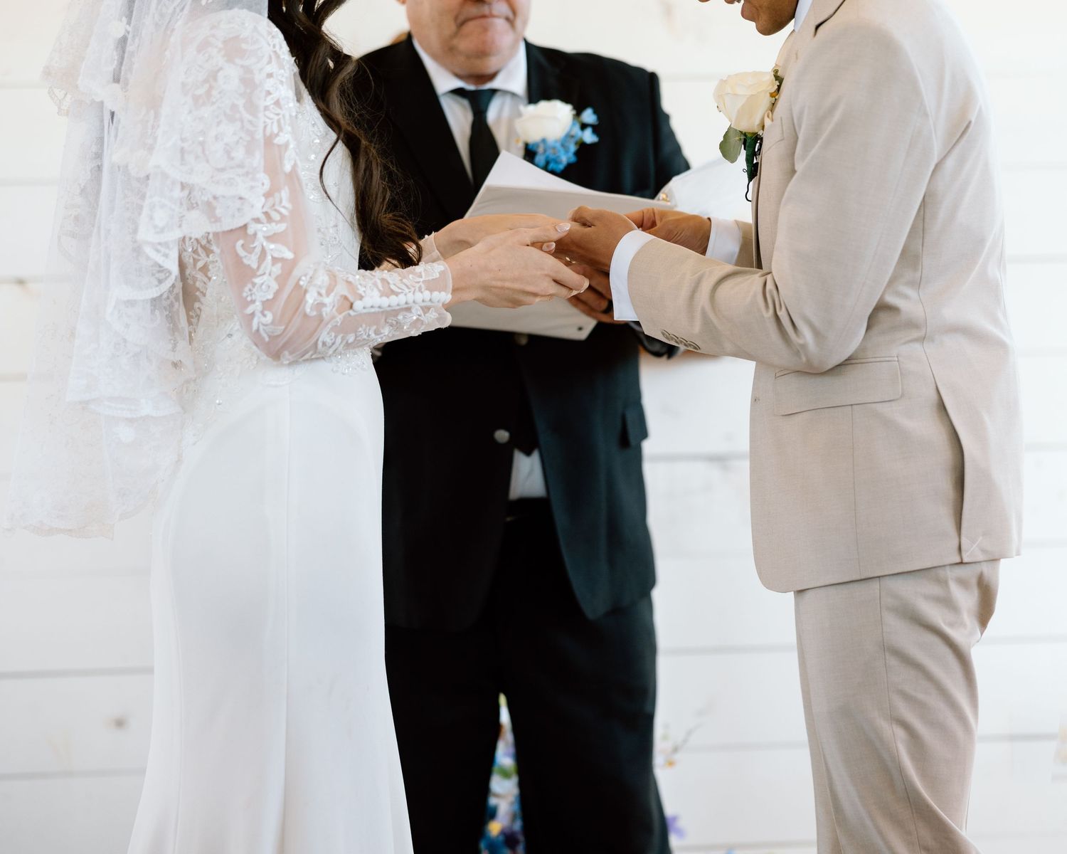 Bride and groom exchanging rings during wedding ceremony, officiant standing behind them.