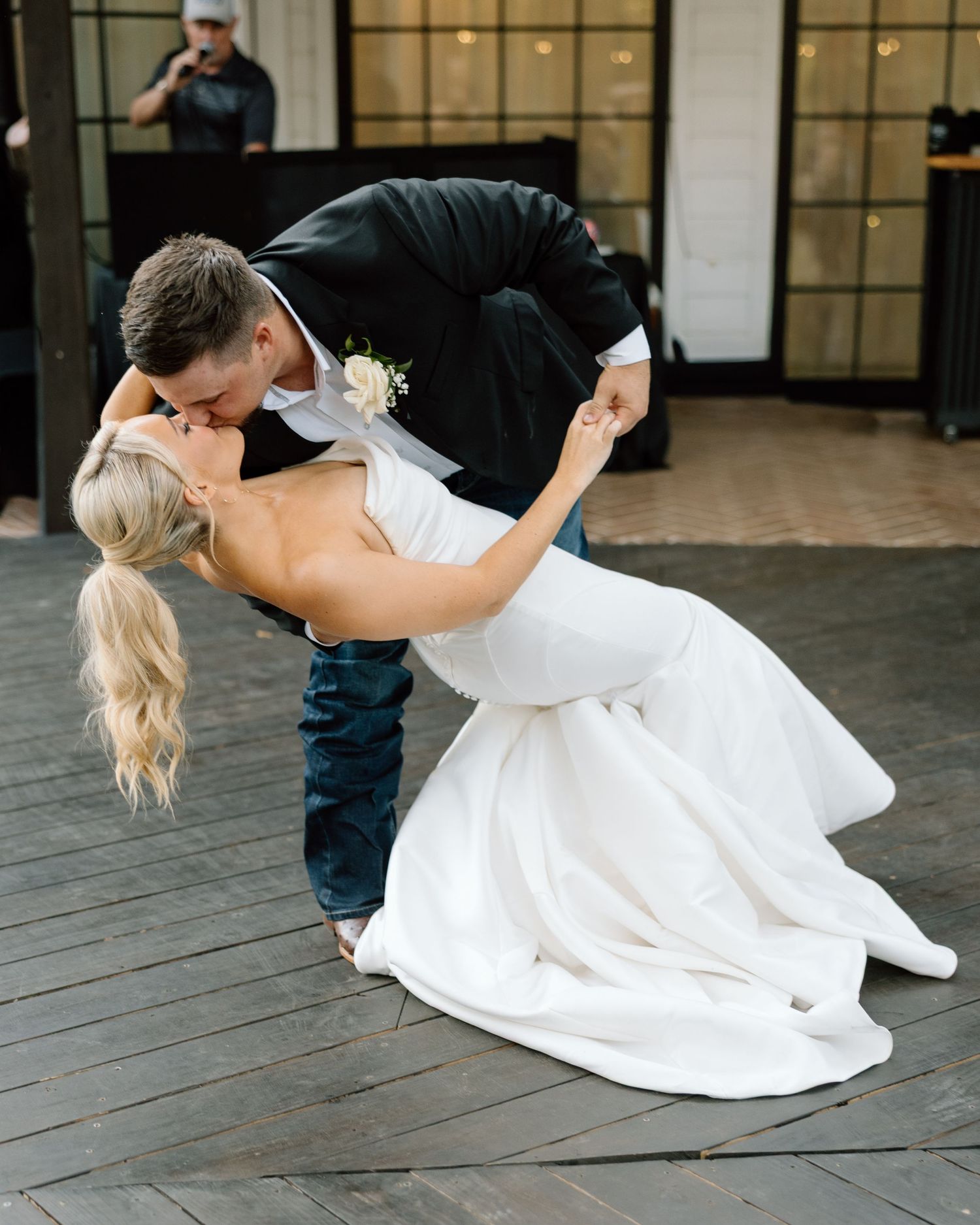 Groom in black suit dipping bride in white wedding gown for a romantic kiss on an outdoor dance floor.