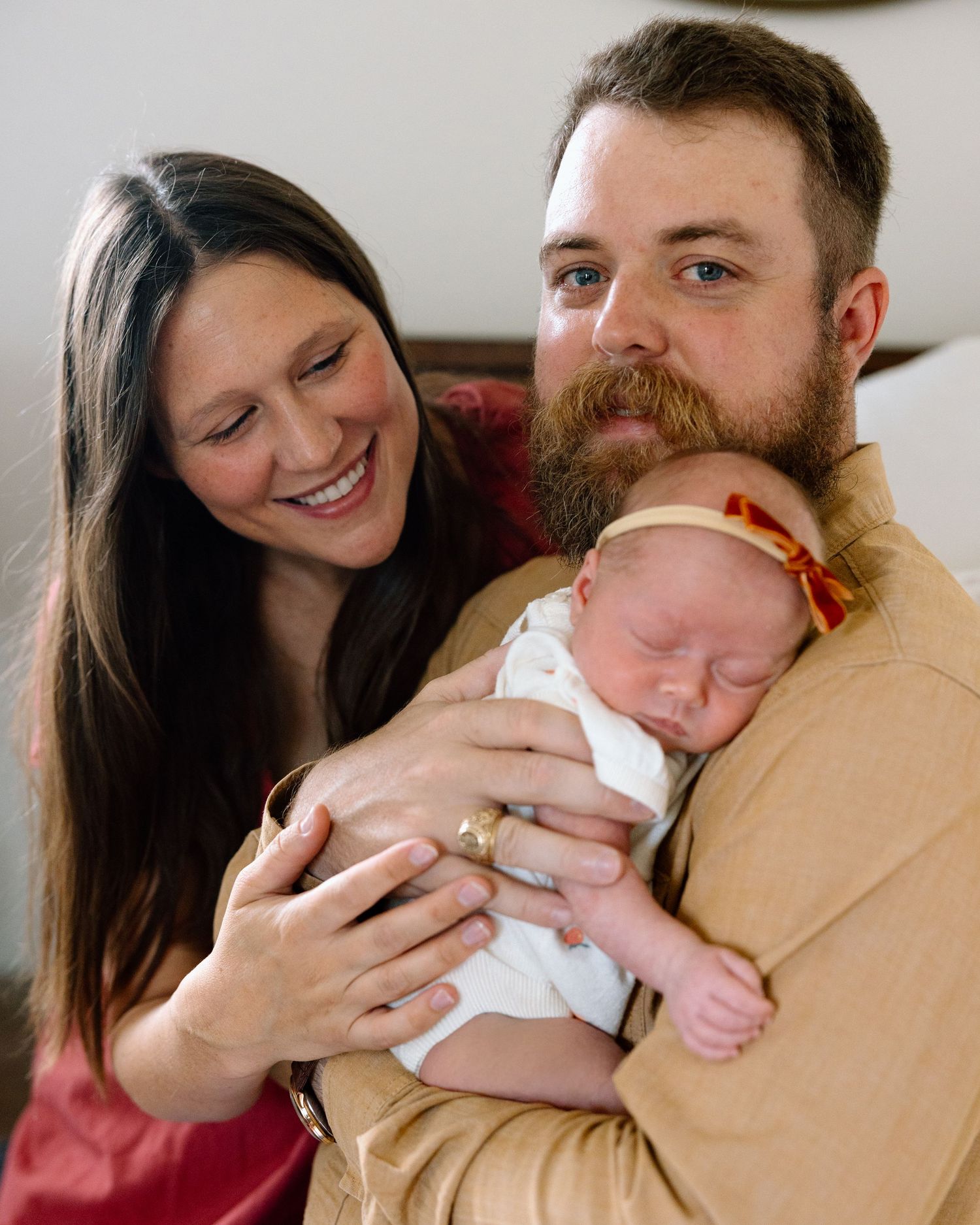 Smiling couple holding their newborn baby, with the bearded father cradling the infant in a warm family portrait.