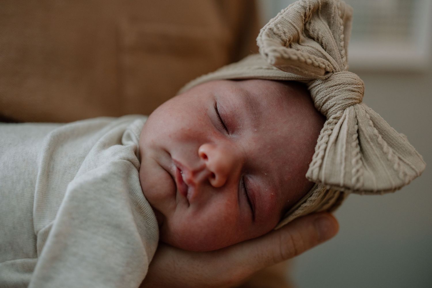 Peaceful sleeping newborn wearing a beige bow headband.
