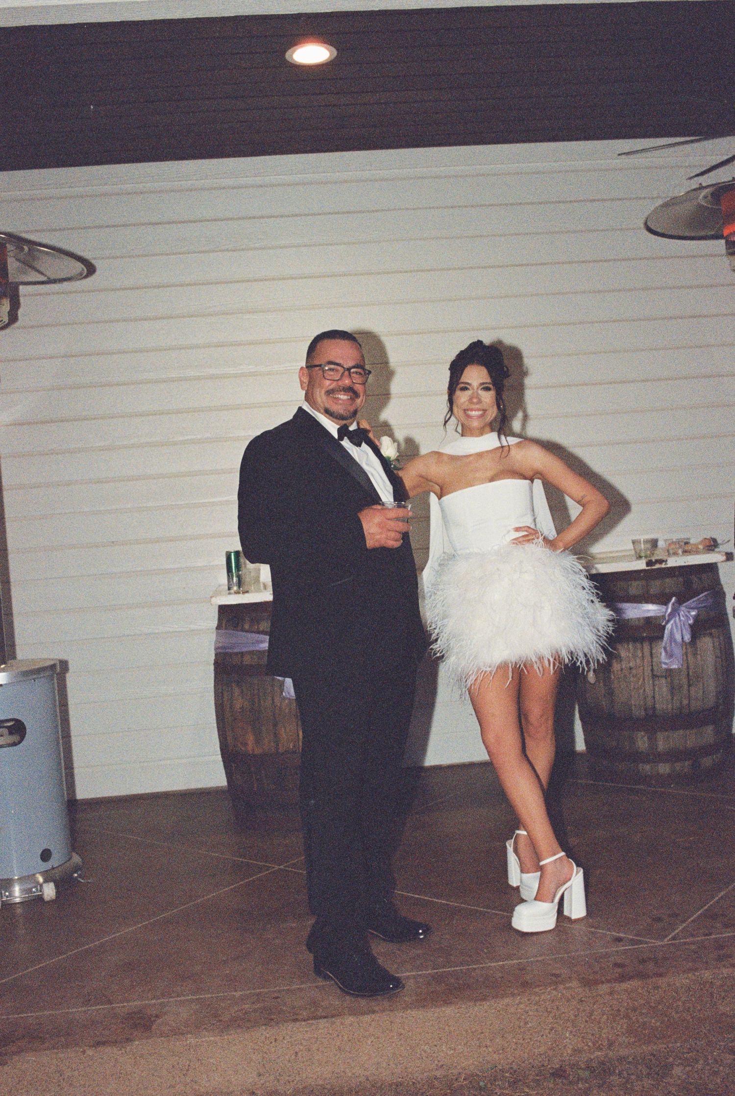 A celebratory moment at a wedding reception with two people posing near wooden barrels.