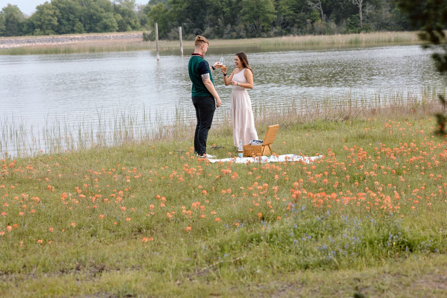 A couple sharing a tender moment in a meadow filled with orange wildflowers beside a lake.