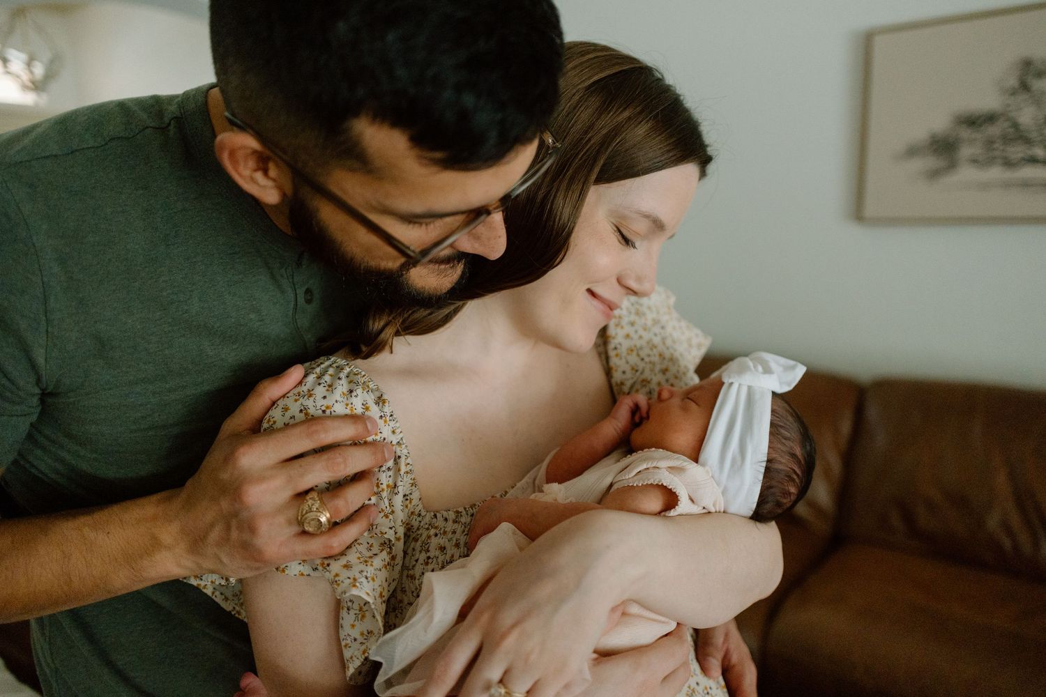 An intimate family moment shared on a couch while holding a newborn in white clothing.