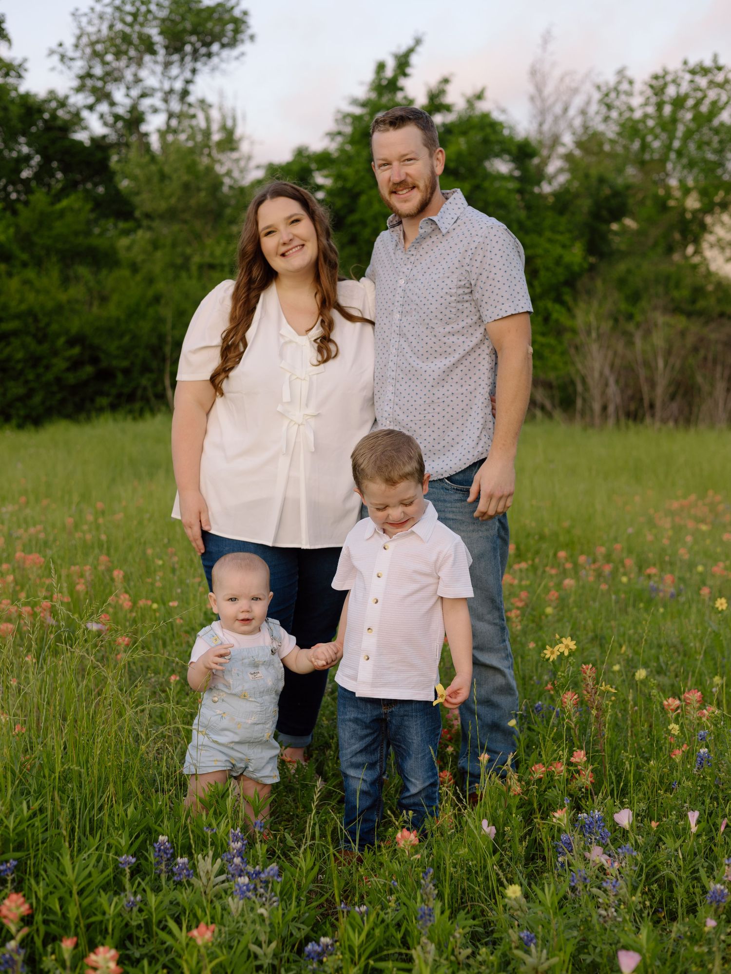 Family posed together in a wildflower meadow with tall grass and blooming bluebonnets in springtime.