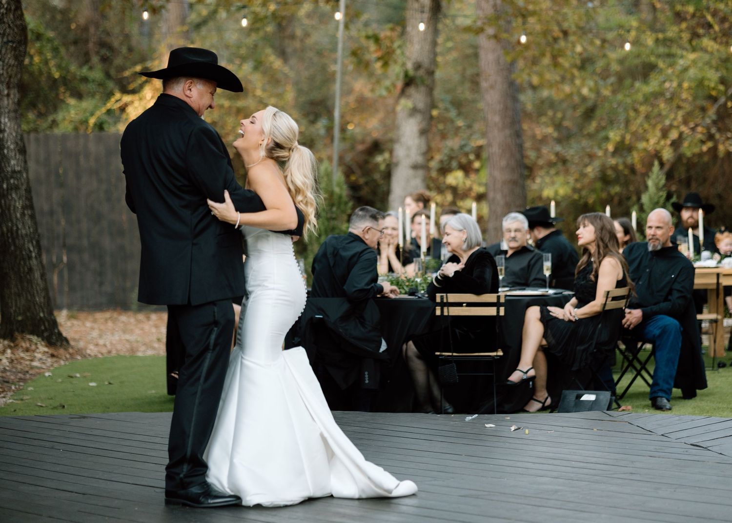 Bride and groom share first dance outdoors at rustic wedding reception with guests seated at decorated tables.