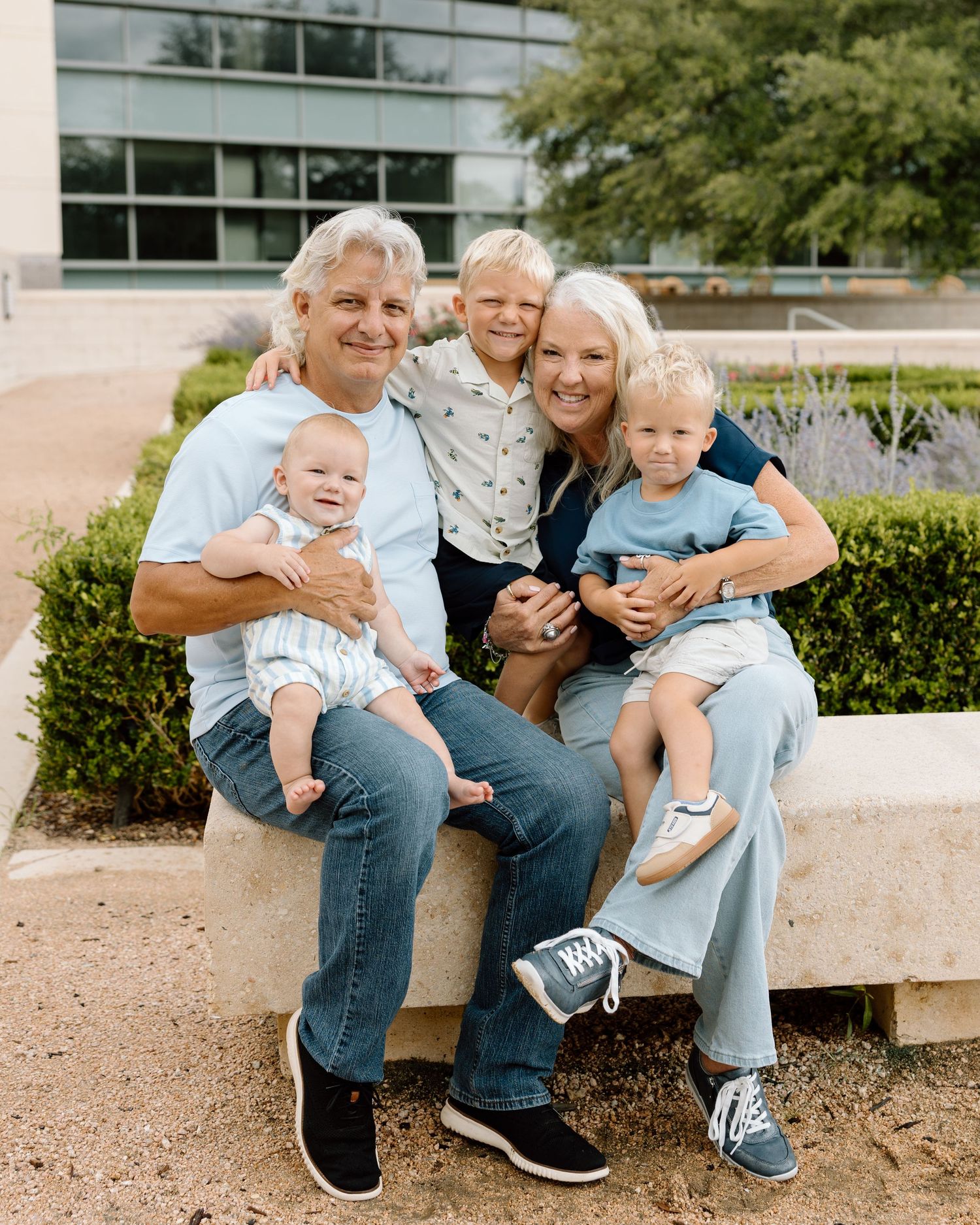 A happy family of five poses outdoors on a stone bench, with two adults holding three young children.