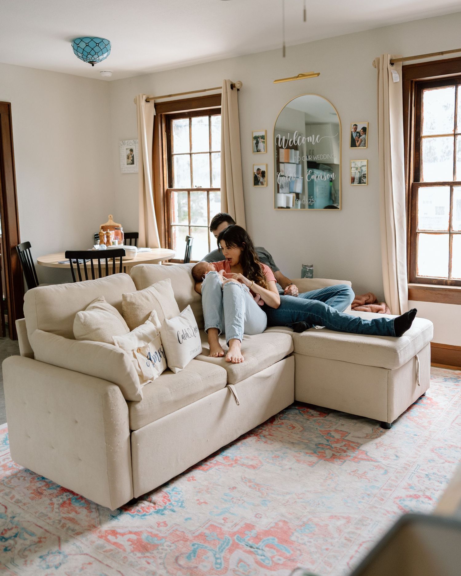 Young family relaxing on a beige sectional sofa in a cozy living room with a colorful rug.