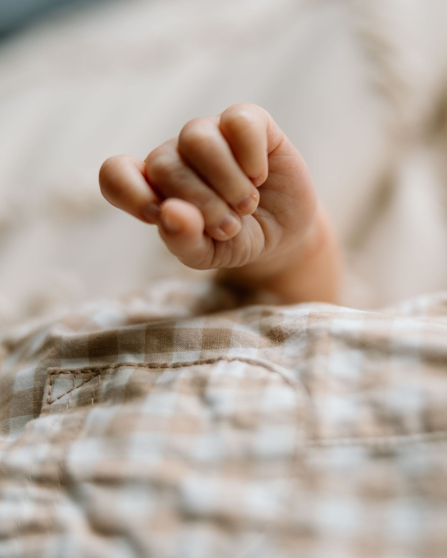Close-up of a newborn baby's tiny clenched fist resting on a soft plaid blanket.