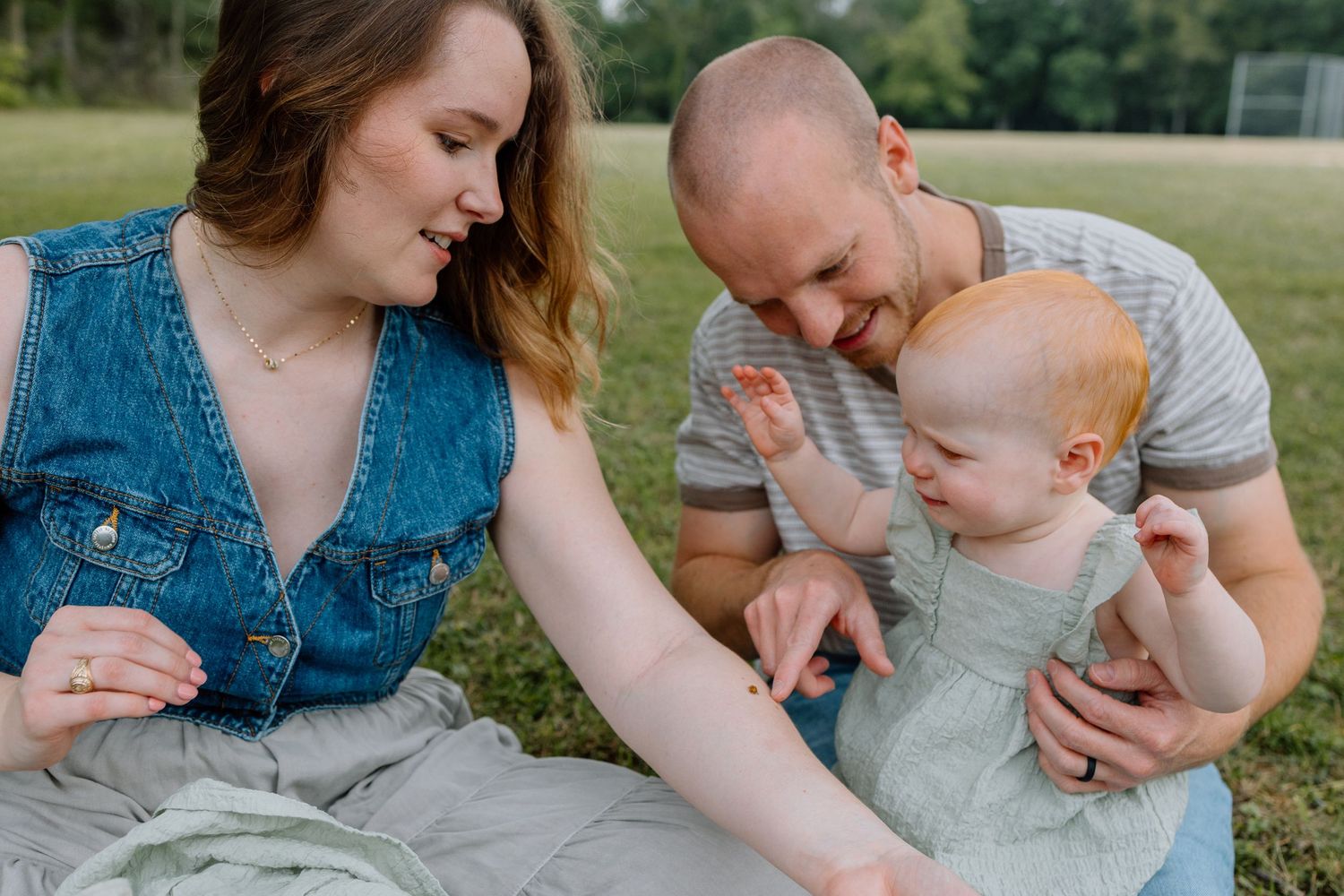 A family sits together on grass during a warm sunny day in an outdoor setting.