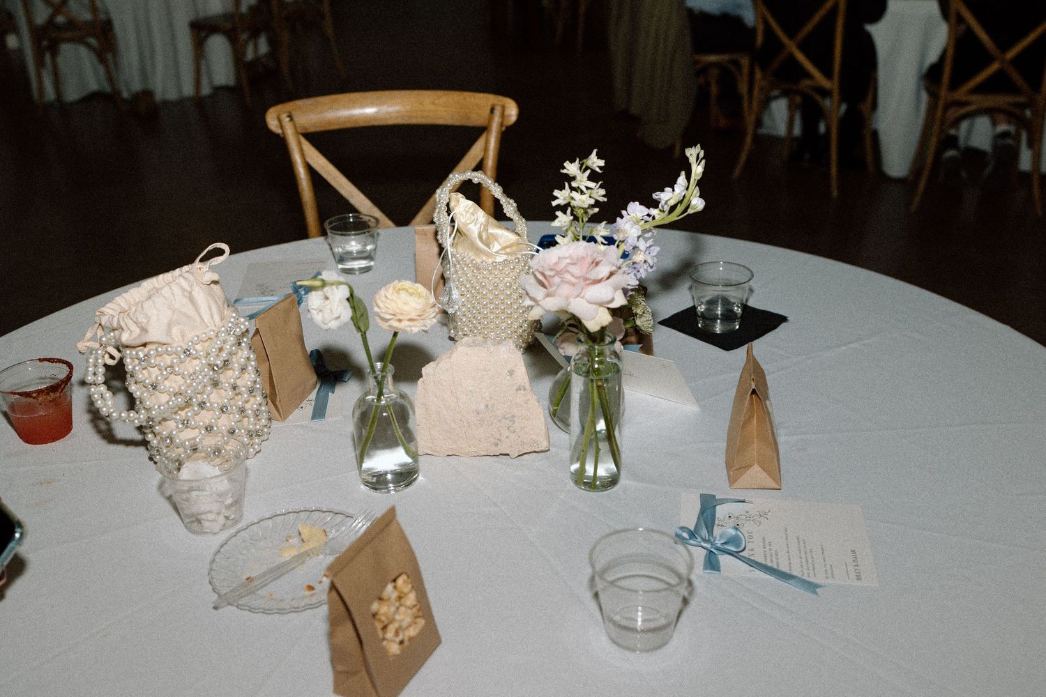 Wedding reception table setting with white linens, woven decor and small floral arrangements.