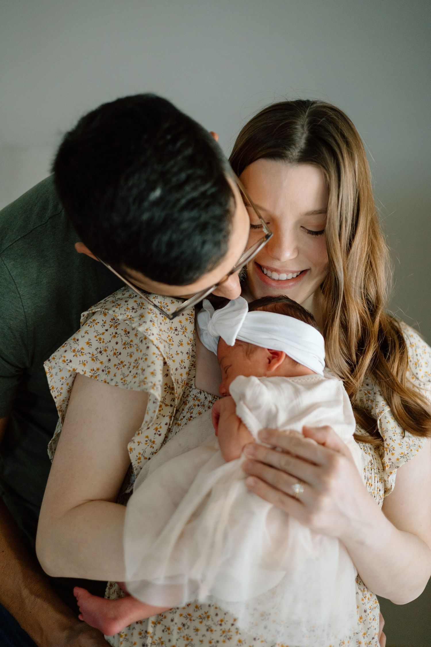 Happy parents sharing intimate moment while holding their newborn baby in white dress.