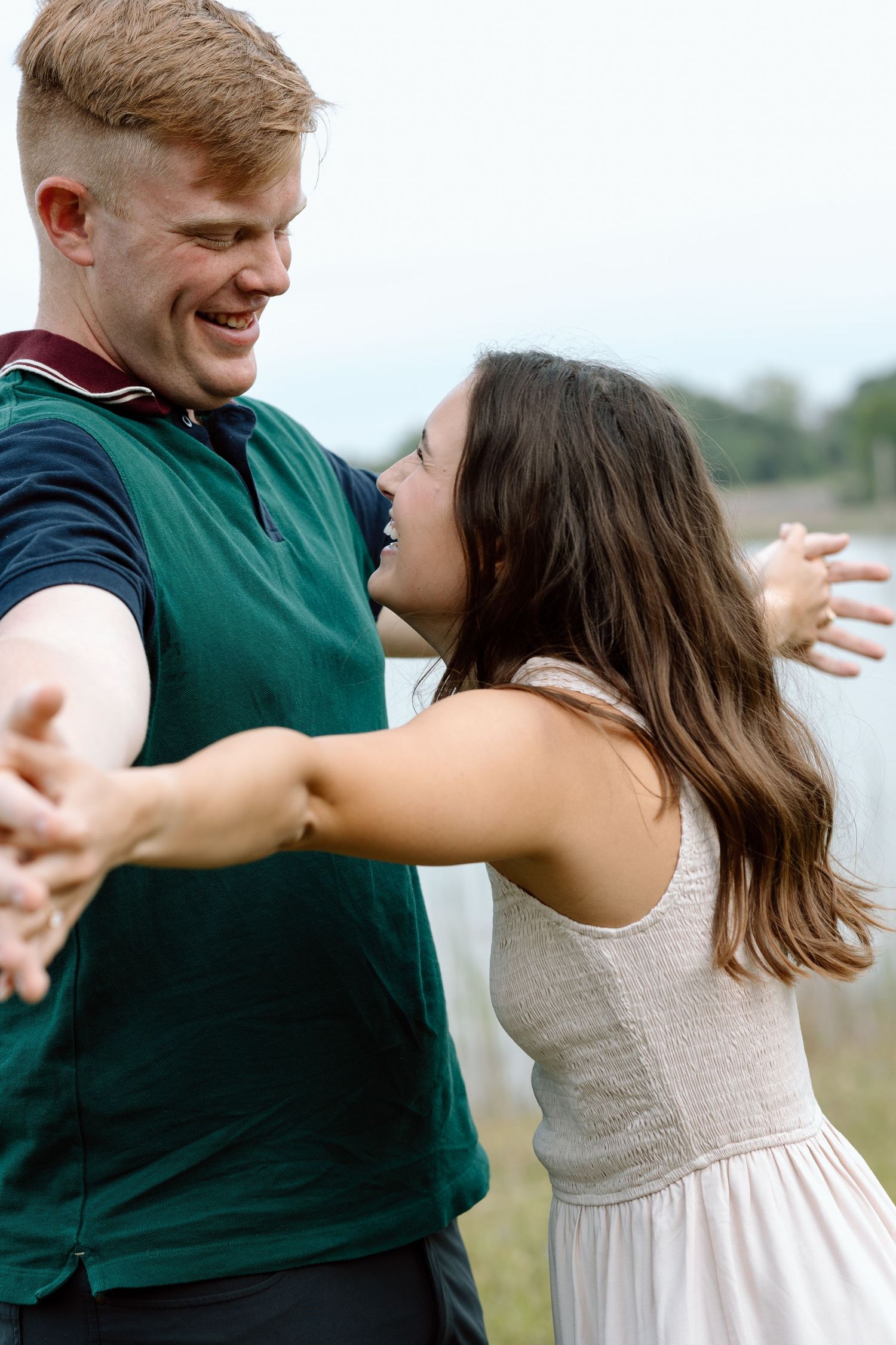 A couple shares a lighthearted dance moment outdoors by a lake.