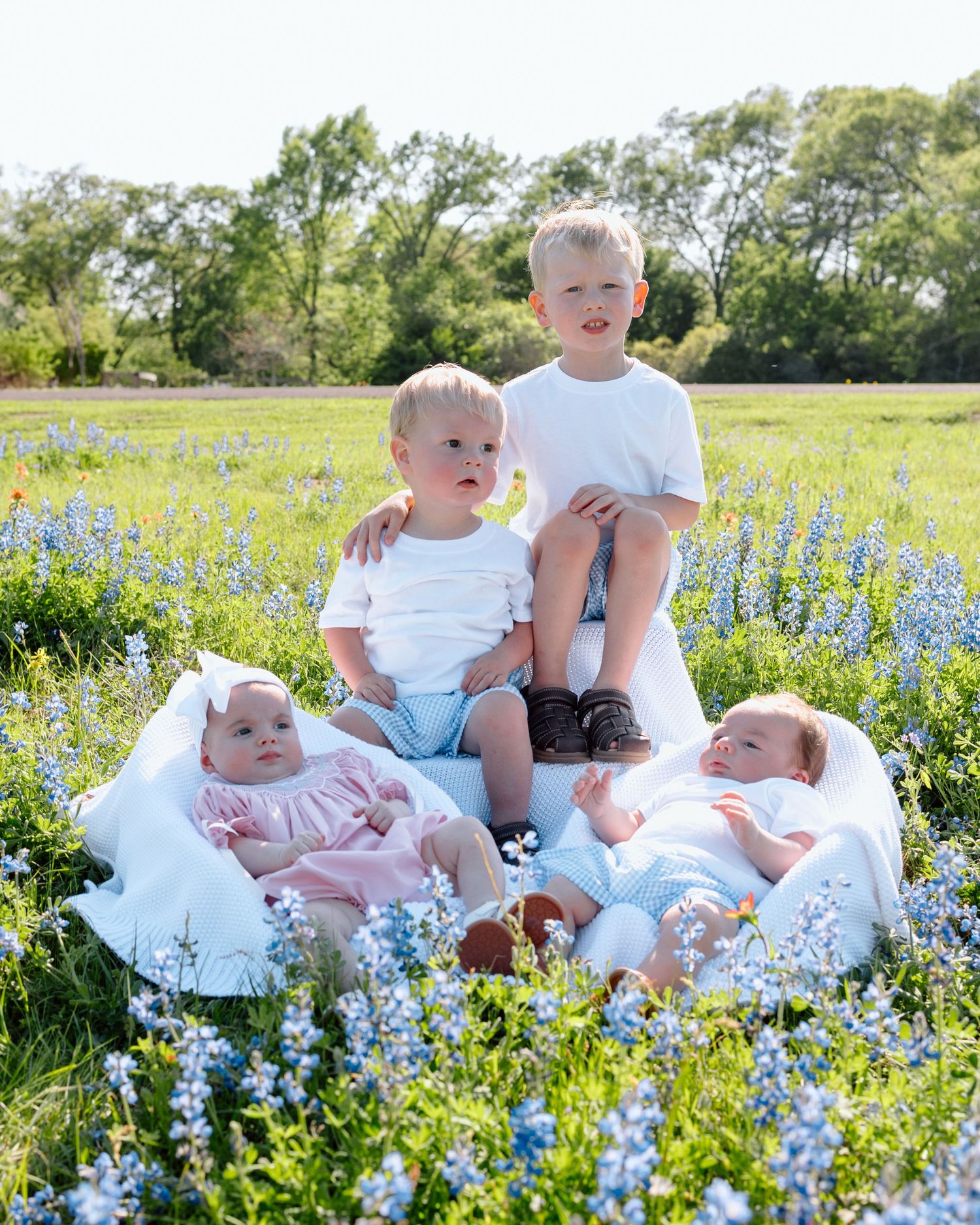 Children sitting together in a field of blooming blue wildflowers on a sunny spring day.