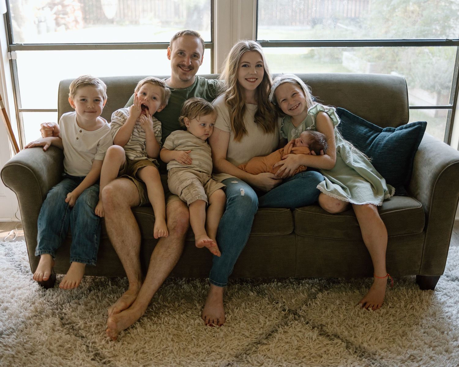 A family relaxes together on a comfortable gray couch in their living room with natural lighting coming through the window.