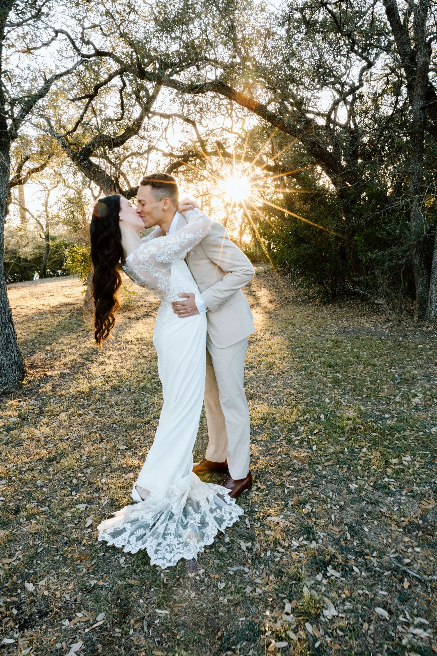 Bride and groom kissing at golden sunset under oak trees in outdoor wedding.