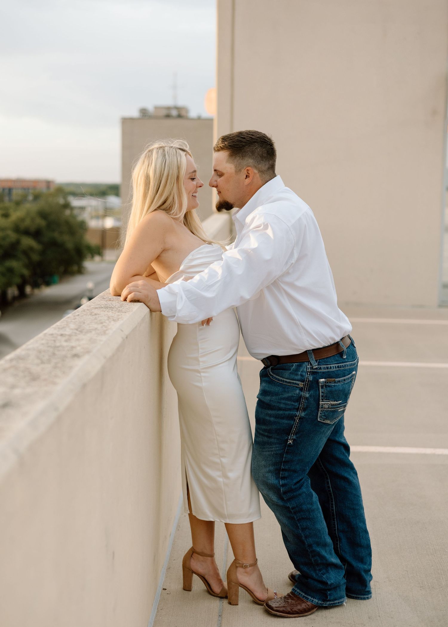 Couple sharing a romantic moment on a rooftop balcony, woman in white dress and man in white shirt and jeans.