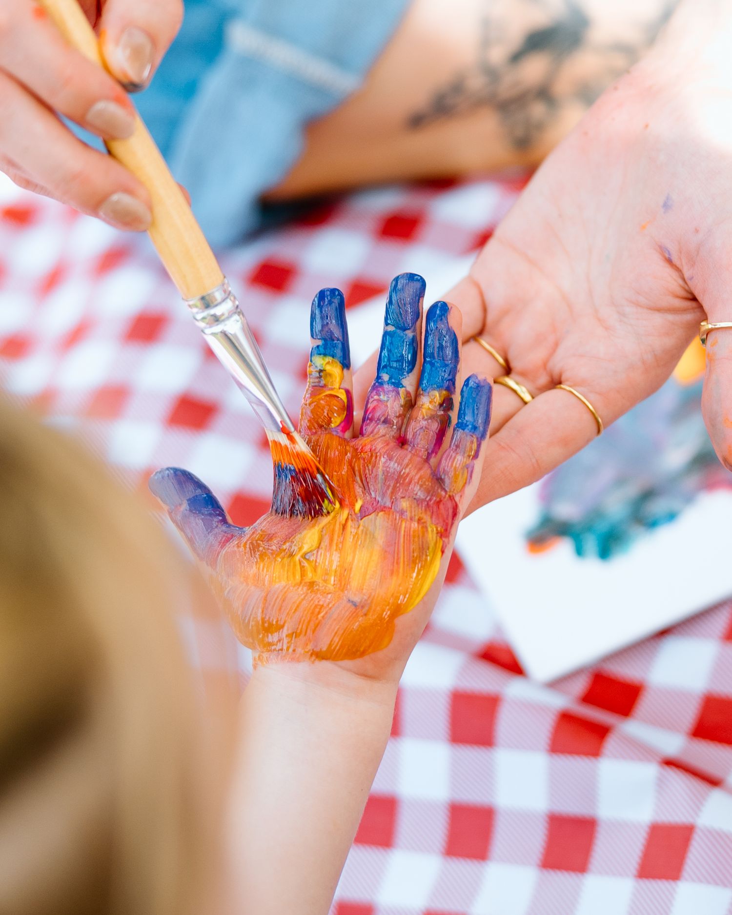 Adult painting colorful blue and orange paint on a child's hand with a brush.