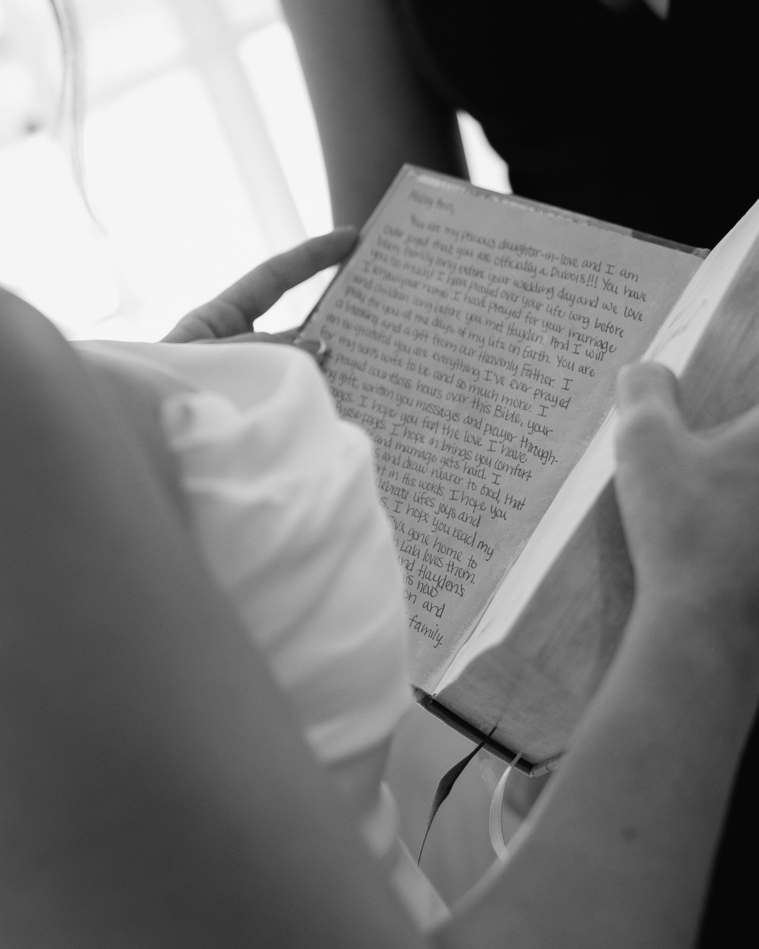 Person reading a handwritten letter in black and white photography, close-up view of pages with cursive writing.
