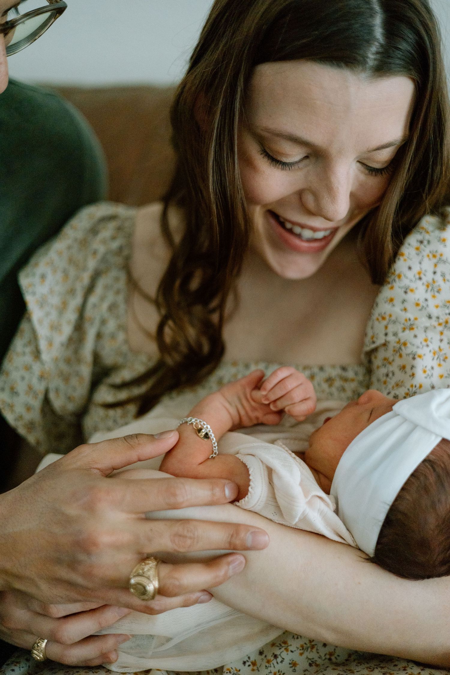 Close-up portrait showing gentle hands cradling a newborn's small feet against a floral dress.