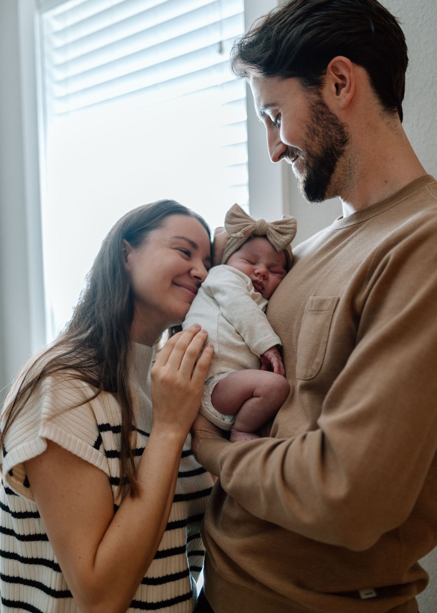 New parents sharing a joyful moment while holding their baby in neutral-toned clothing.