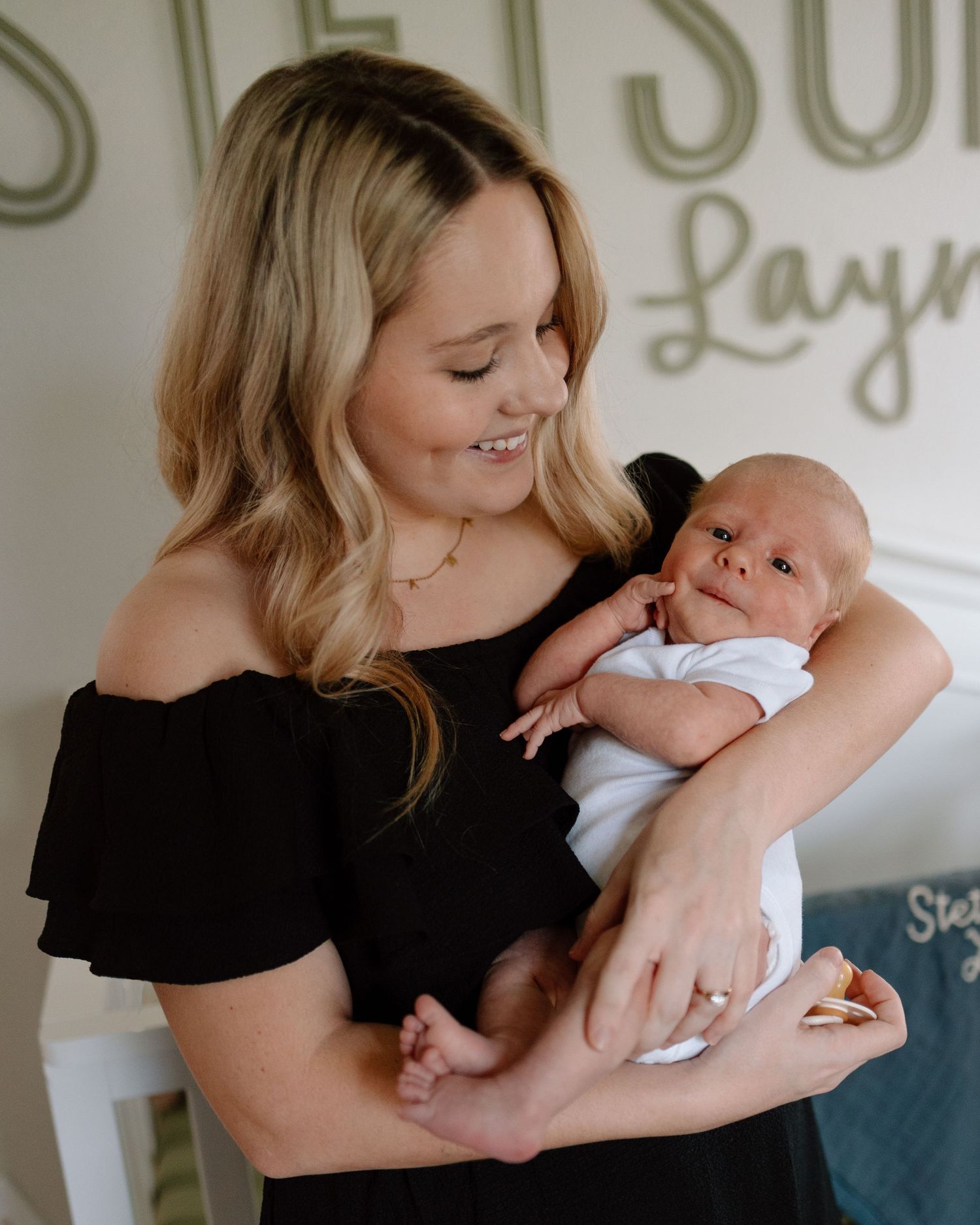 A tender moment captured as a woman in a black off-shoulder top holds a newborn baby in a white onesie.