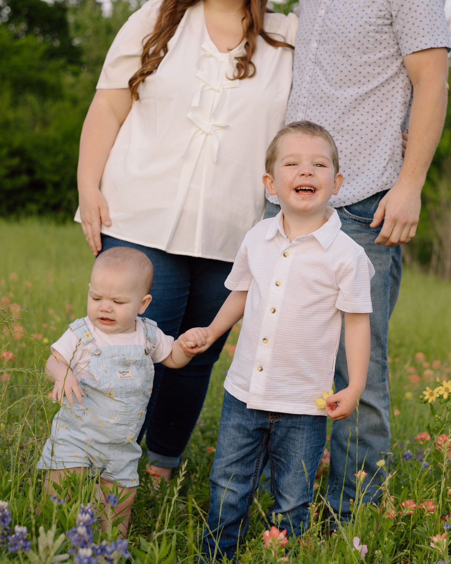 A family outdoors in a meadow with blooming wildflowers, dressed in coordinated light-colored clothing.
