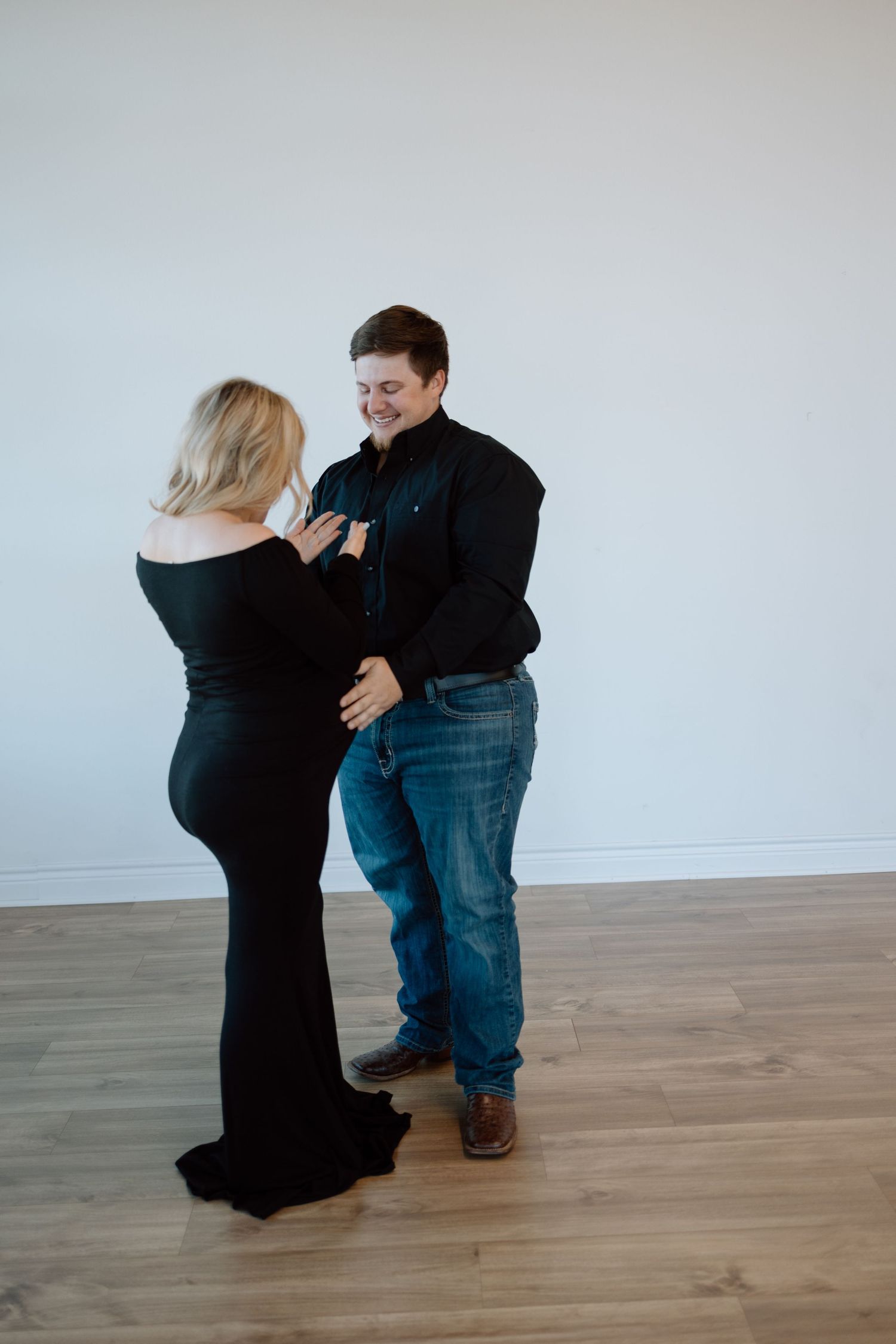 A couple shares an intimate moment while dancing together in a minimalist room with wooden flooring.