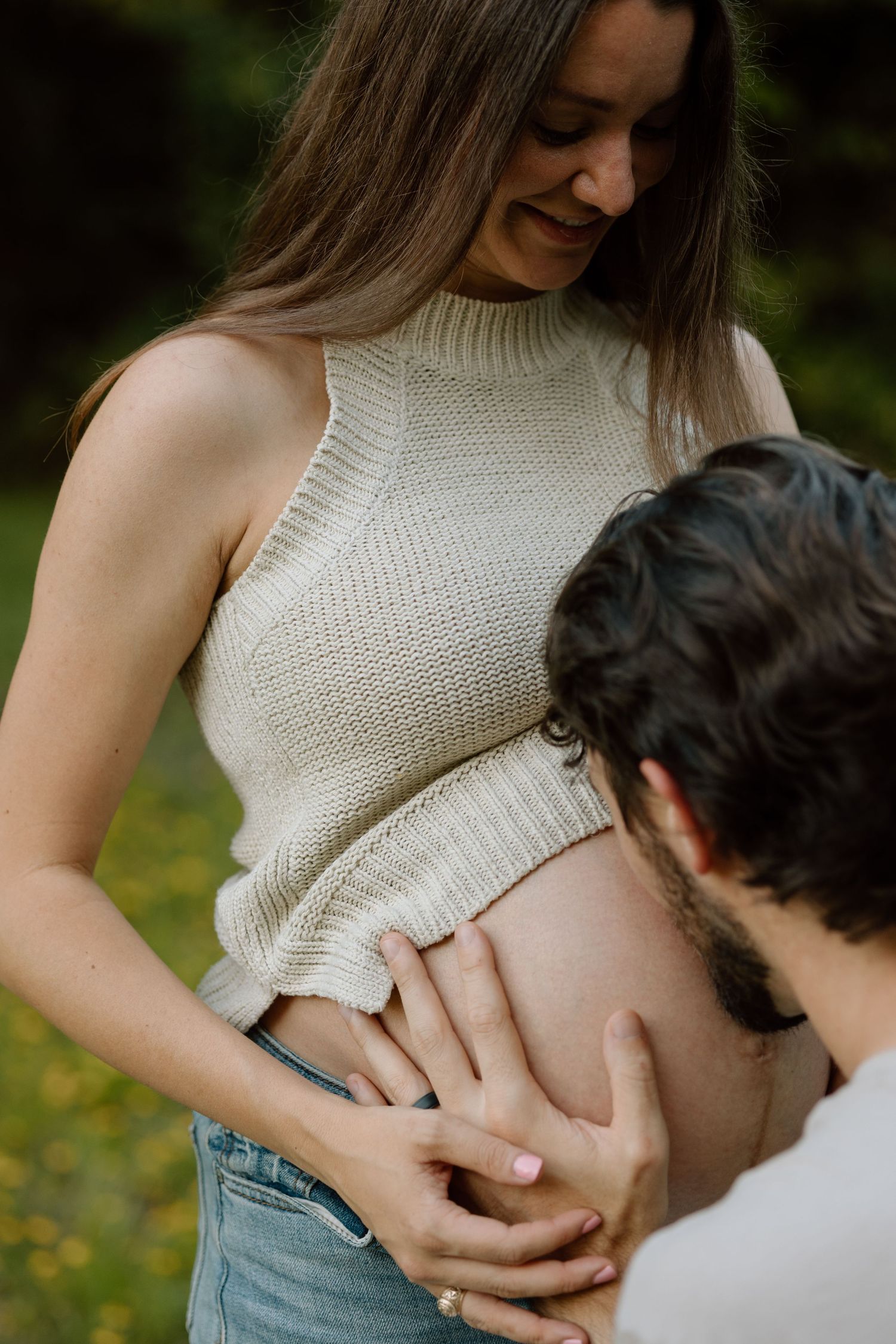 Intimate maternity moment captured with couple and baby bump in white knit sweater outdoors.