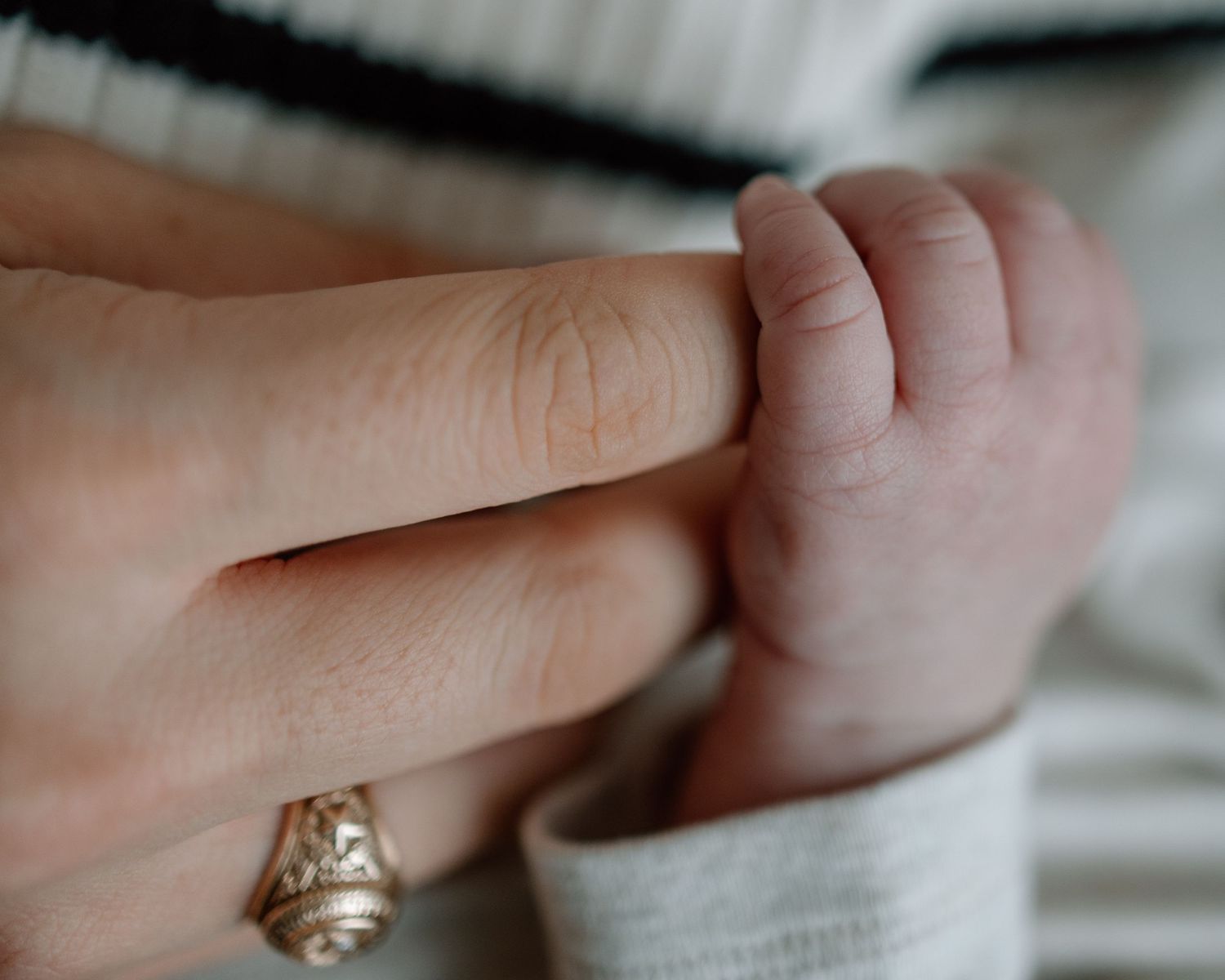 Close-up of baby's tiny hand grasping adult finger with engagement ring visible.