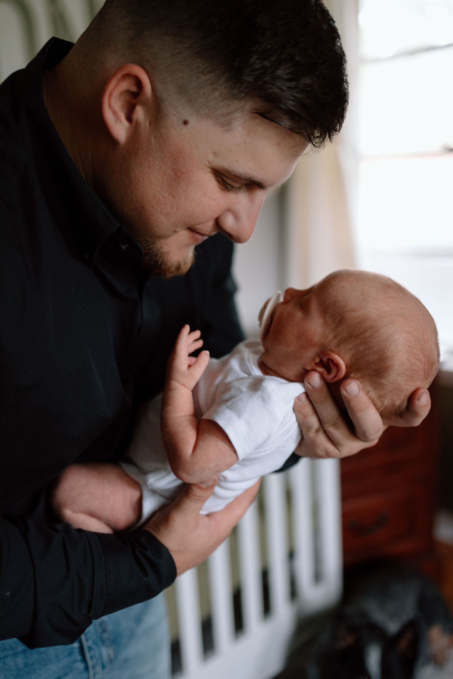A tender moment as someone in a black sweater and jeans cradles a newborn baby wearing white.