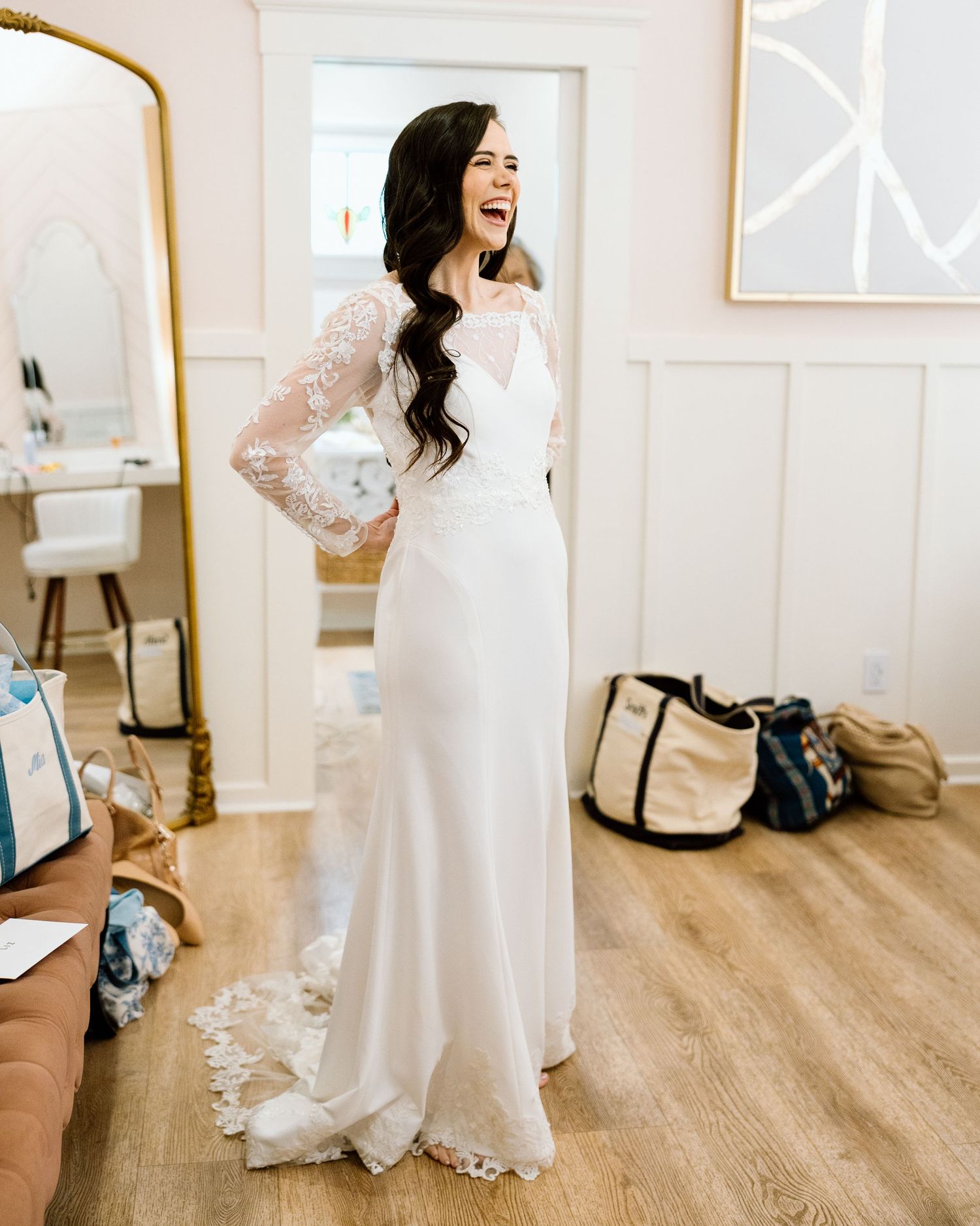 Smiling bride in a white lace long-sleeve wedding gown posing in a bridal boutique fitting room.