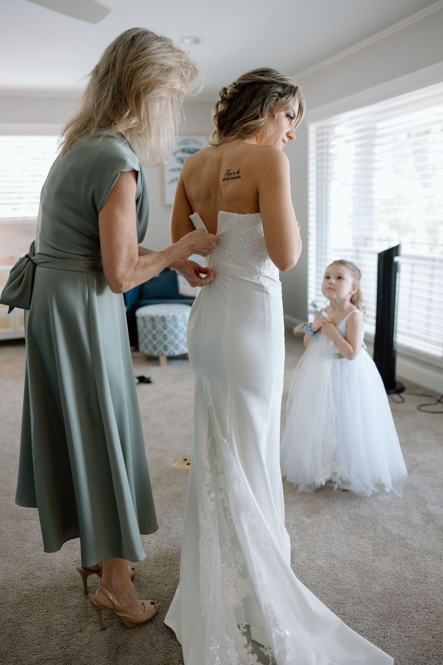 Wedding dress preparations with attendants in a bright room.