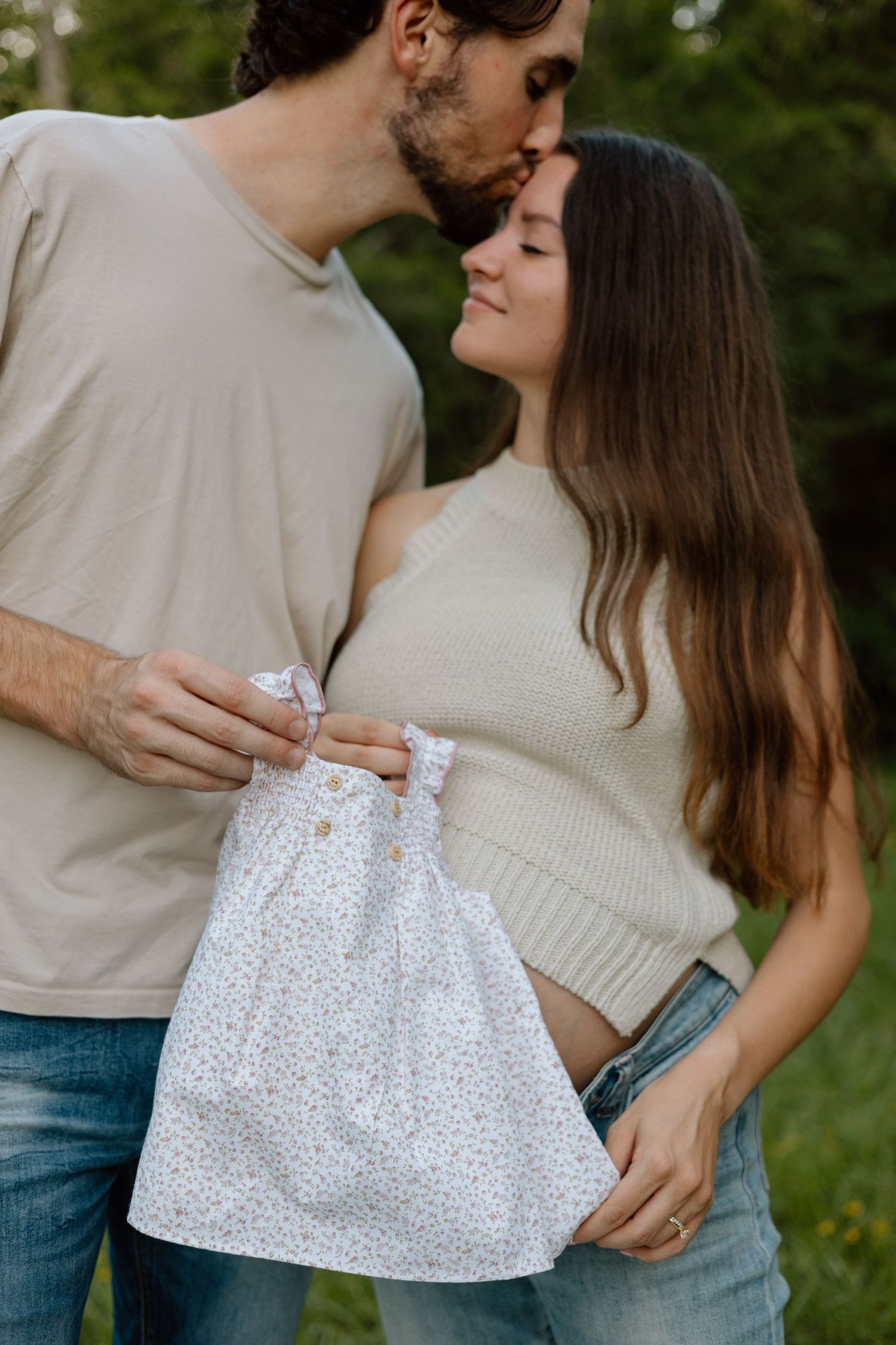 A couple holding a white polka dot dress during an outdoor maternity photo session.