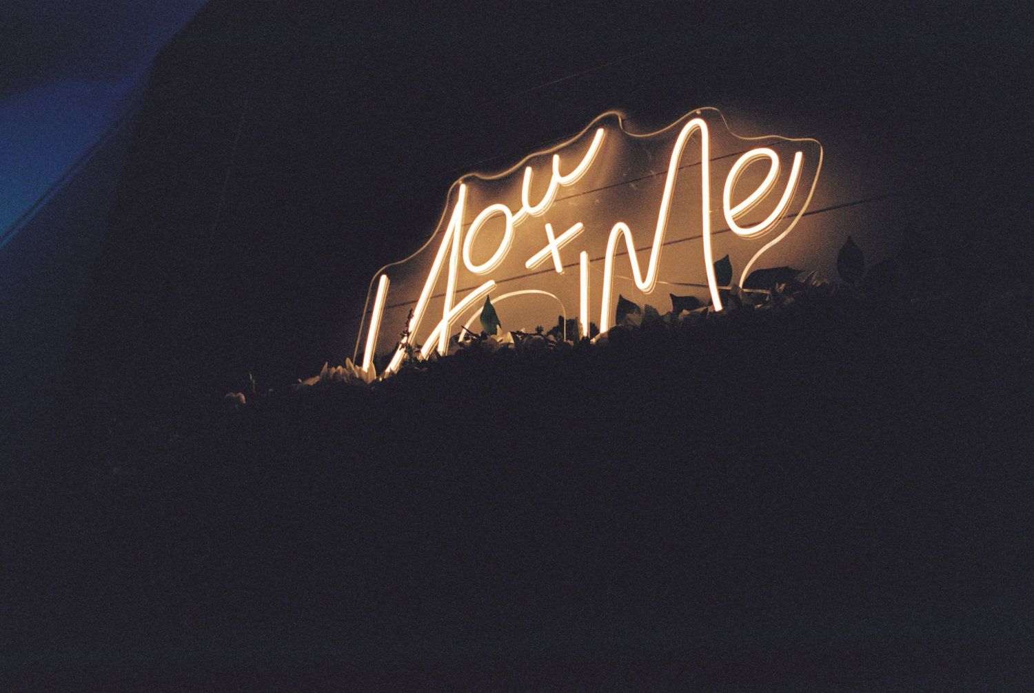 A glowing neon sign reading 'You + Me' in cursive text against a dark background.