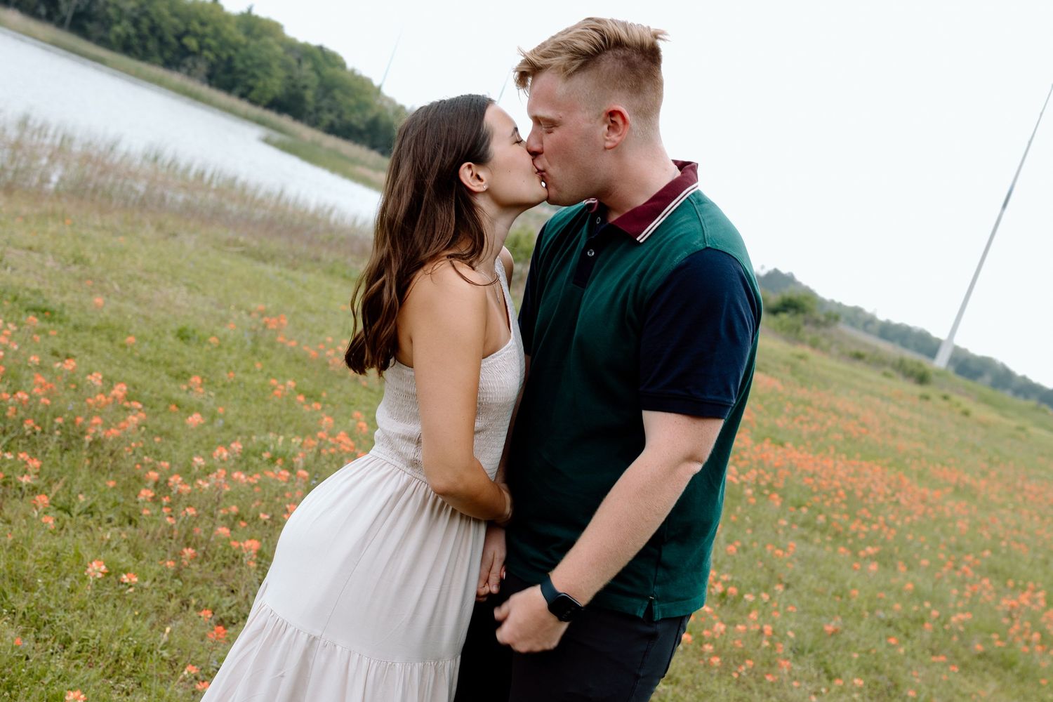 A romantic moment between a couple in a field with a lake in the background.