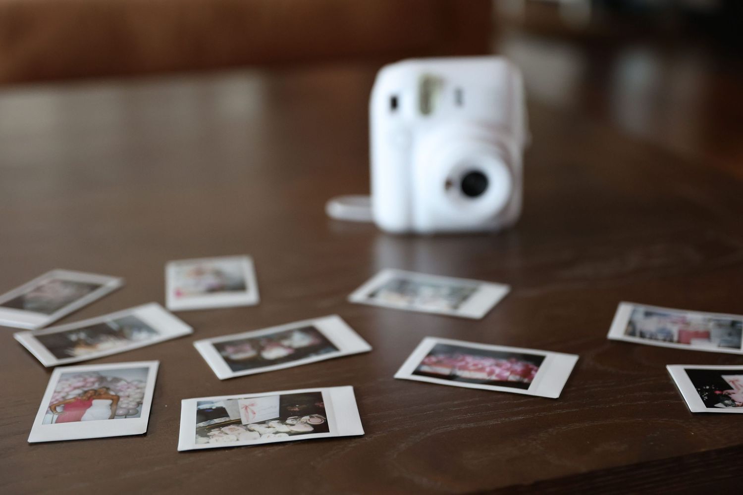 Polaroid instant camera with scattered instant photos on a wooden table surface.