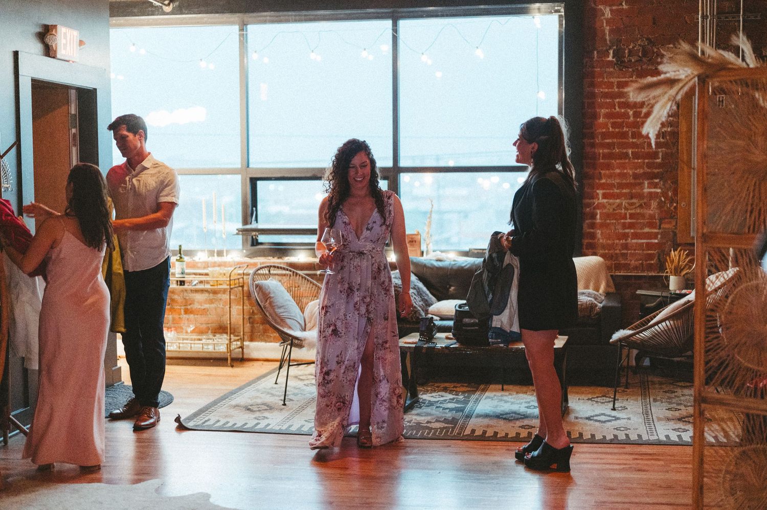 Party guests mingling in an industrial loft space with large windows.