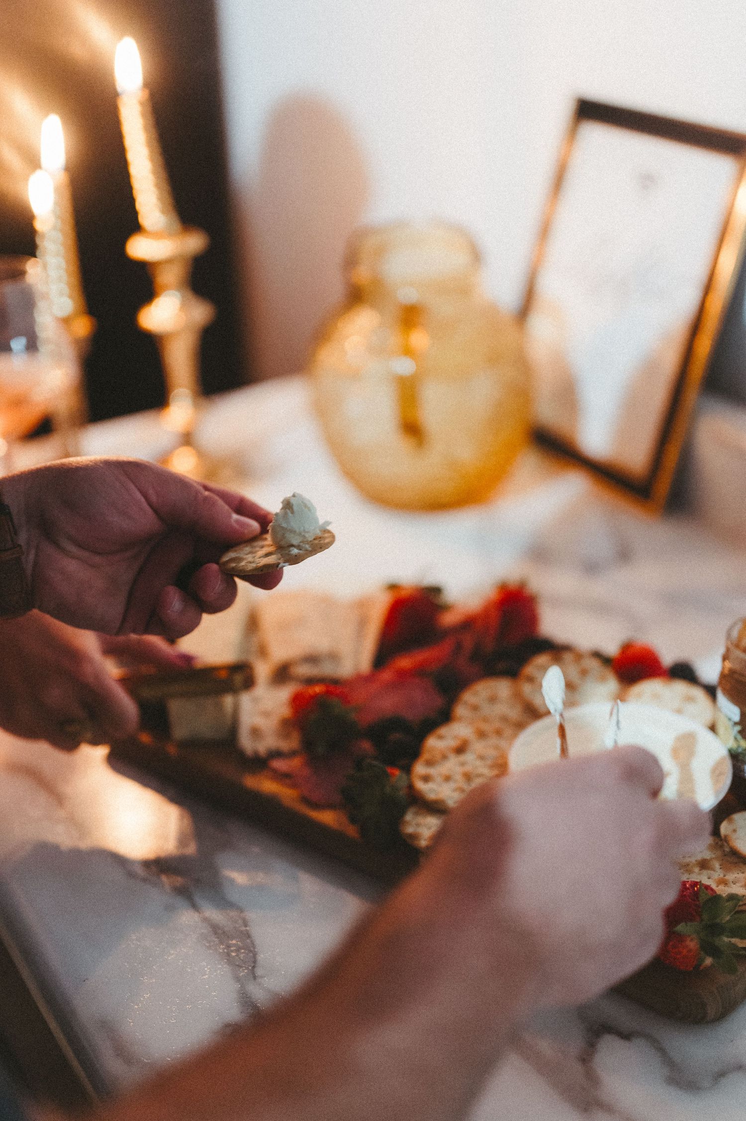 Hands arranging food on a serving board with candlelight and decorative amber glass jar.