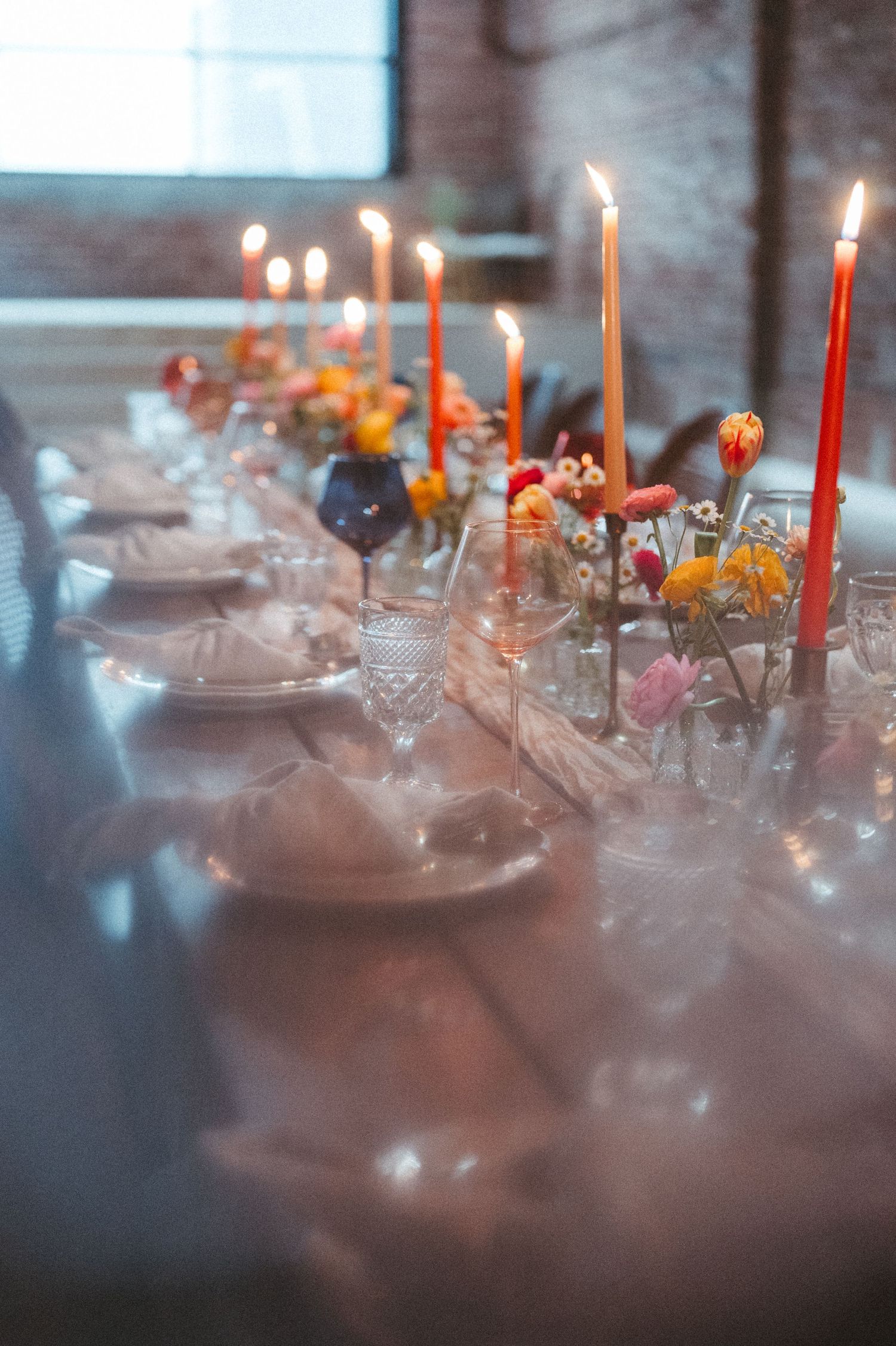 Close-up of table setting with lit candles, floral arrangements and crystal glassware in moody lighting.