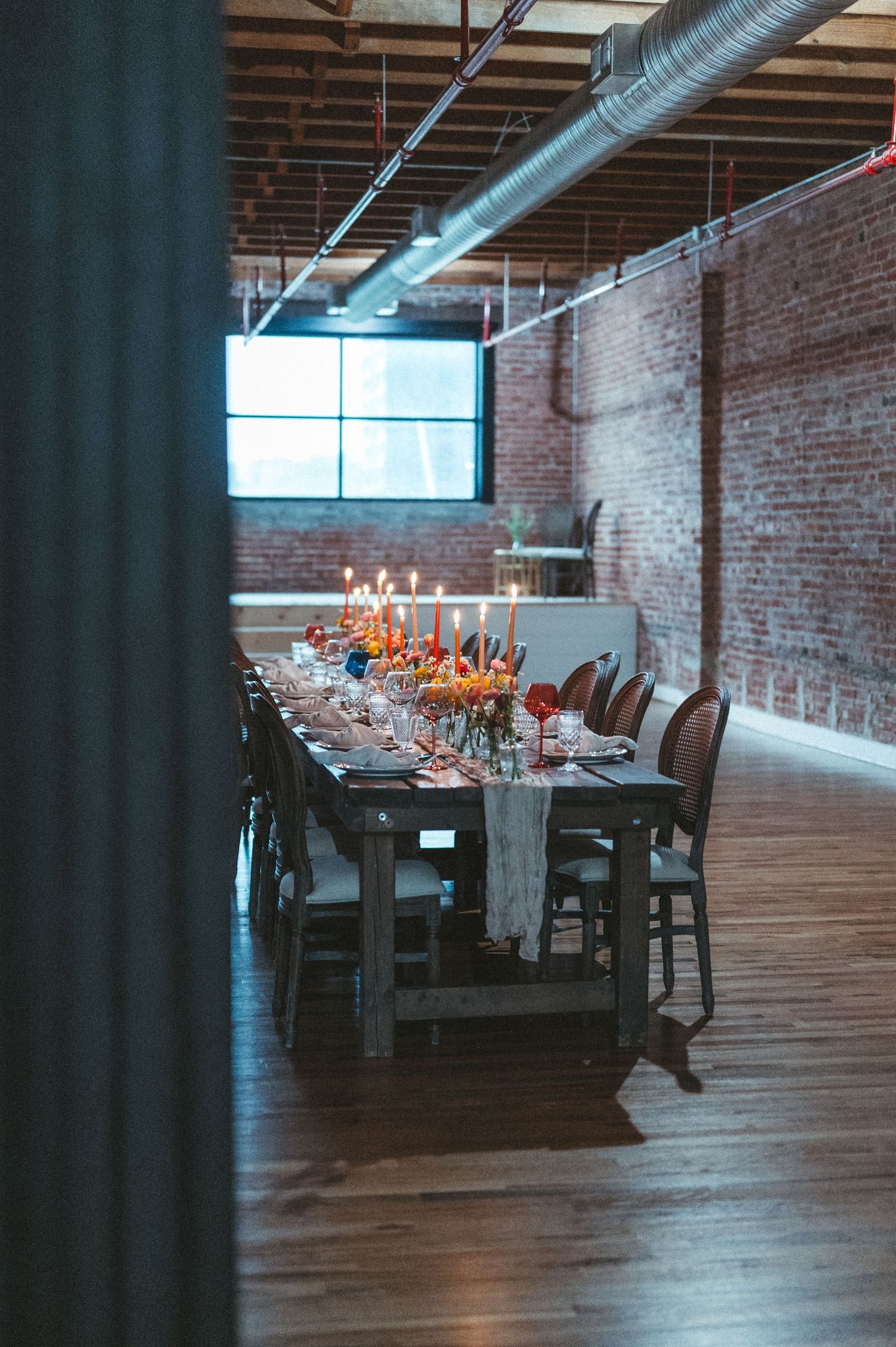 Elegant dining table setup in a rustic brick-walled venue with exposed ductwork and natural lighting.